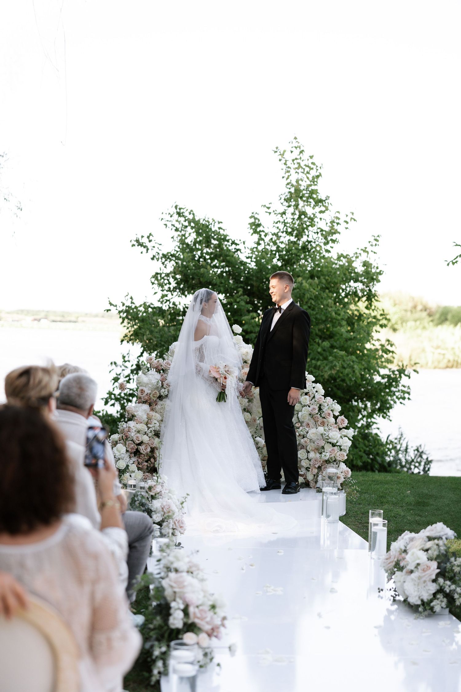 Elegant outdoor wedding ceremony with white floral arch decorations.