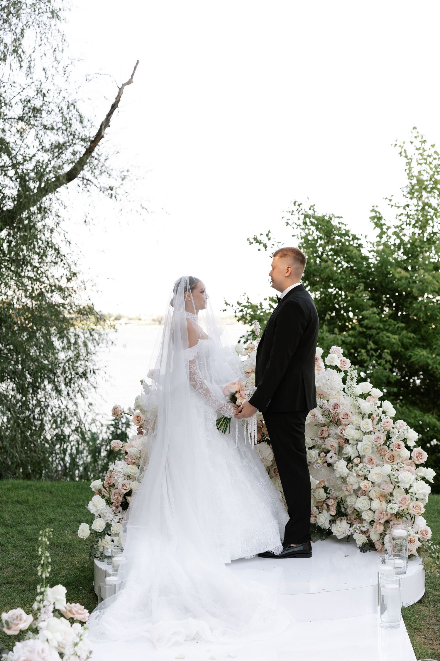Outdoor wedding ceremony setup with white floral arch and elegant decor against natural greenery.