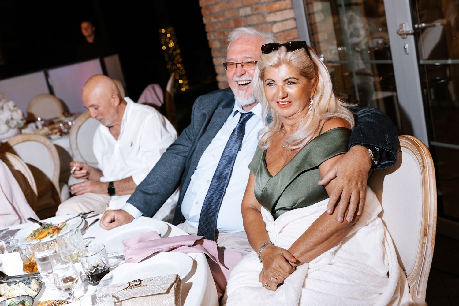 Wedding reception guests enjoying dinner at decorated tables with ambient lighting.
