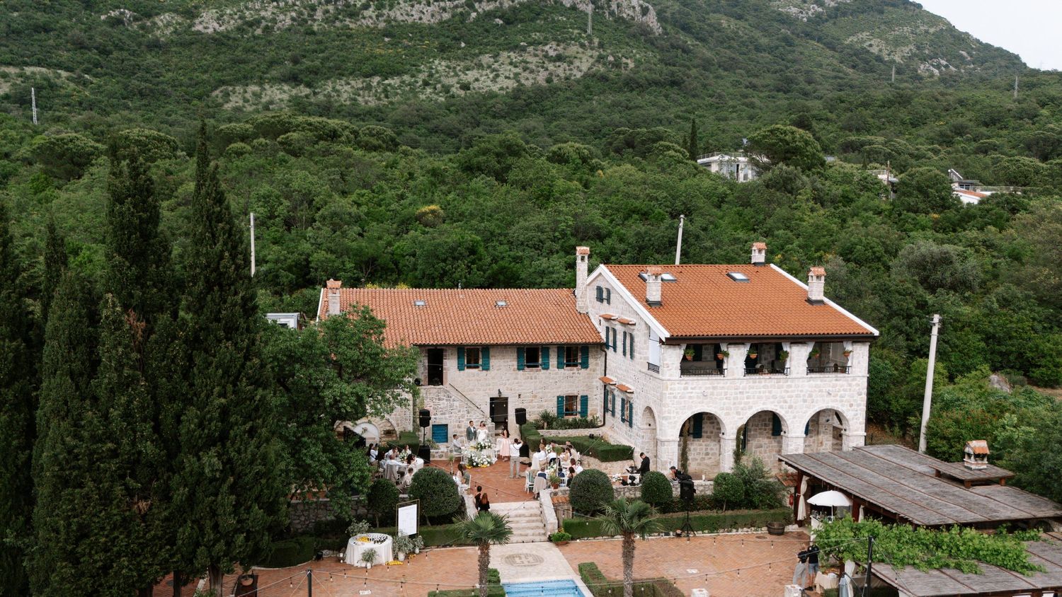 Panoramic view of Mediterranean coastal villas nestled in lush mountainous terrain with red-tiled roofs and stone architecture.