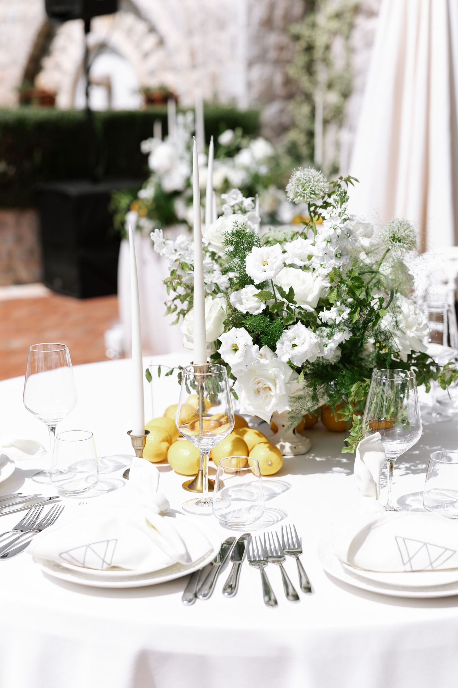 Elegant white table setting with fresh flowers and lemons at an outdoor wedding reception.