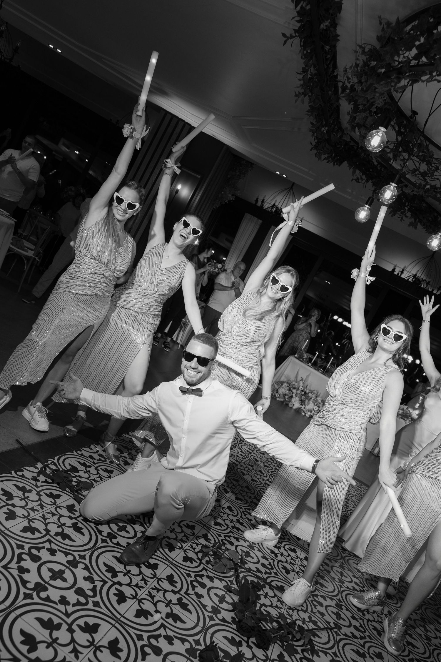 A group of people in matching outfits strike dramatic dance poses during a black and white party photo.