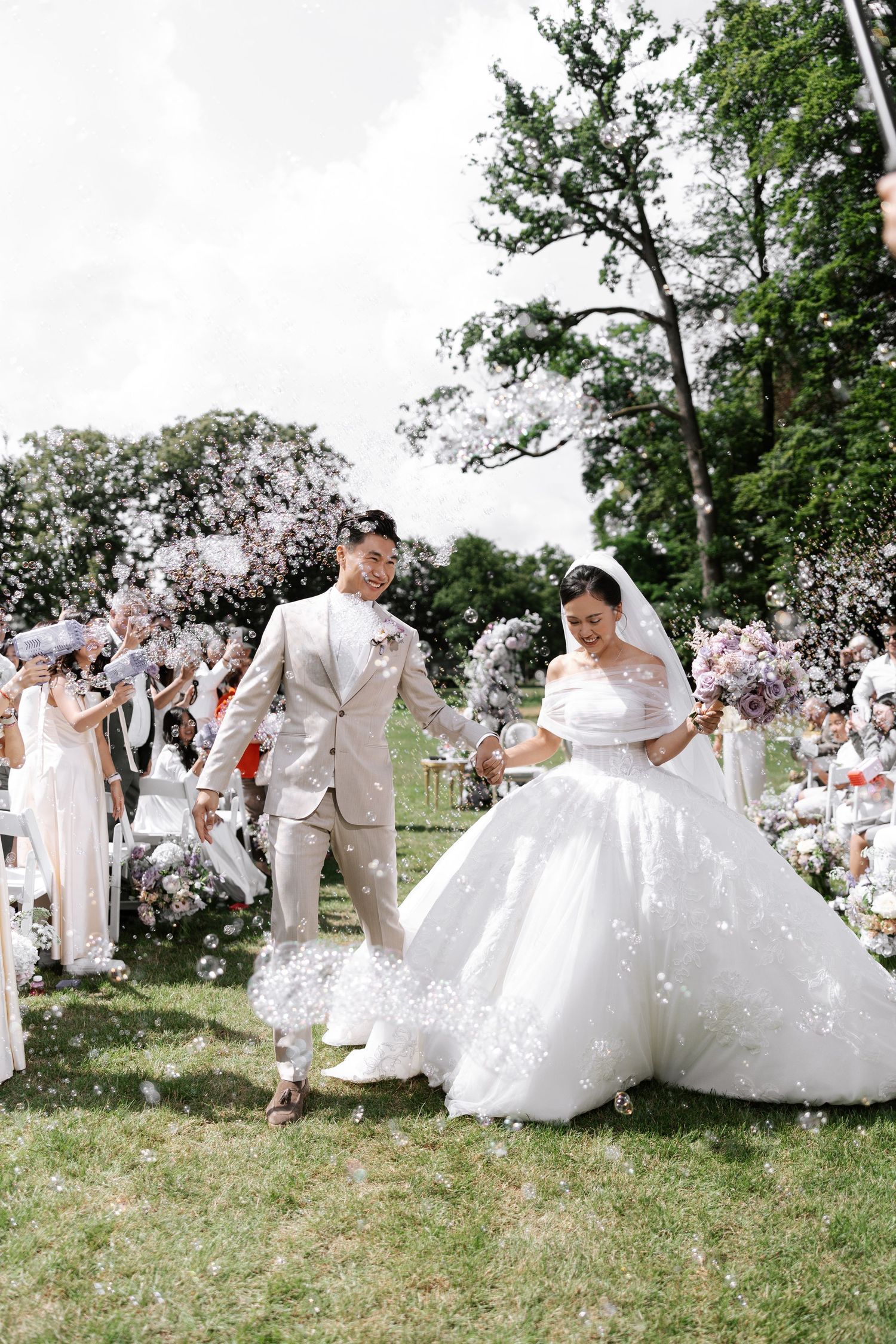 Couples in white wedding attire dancing together on a grassy hillside during an outdoor celebration.