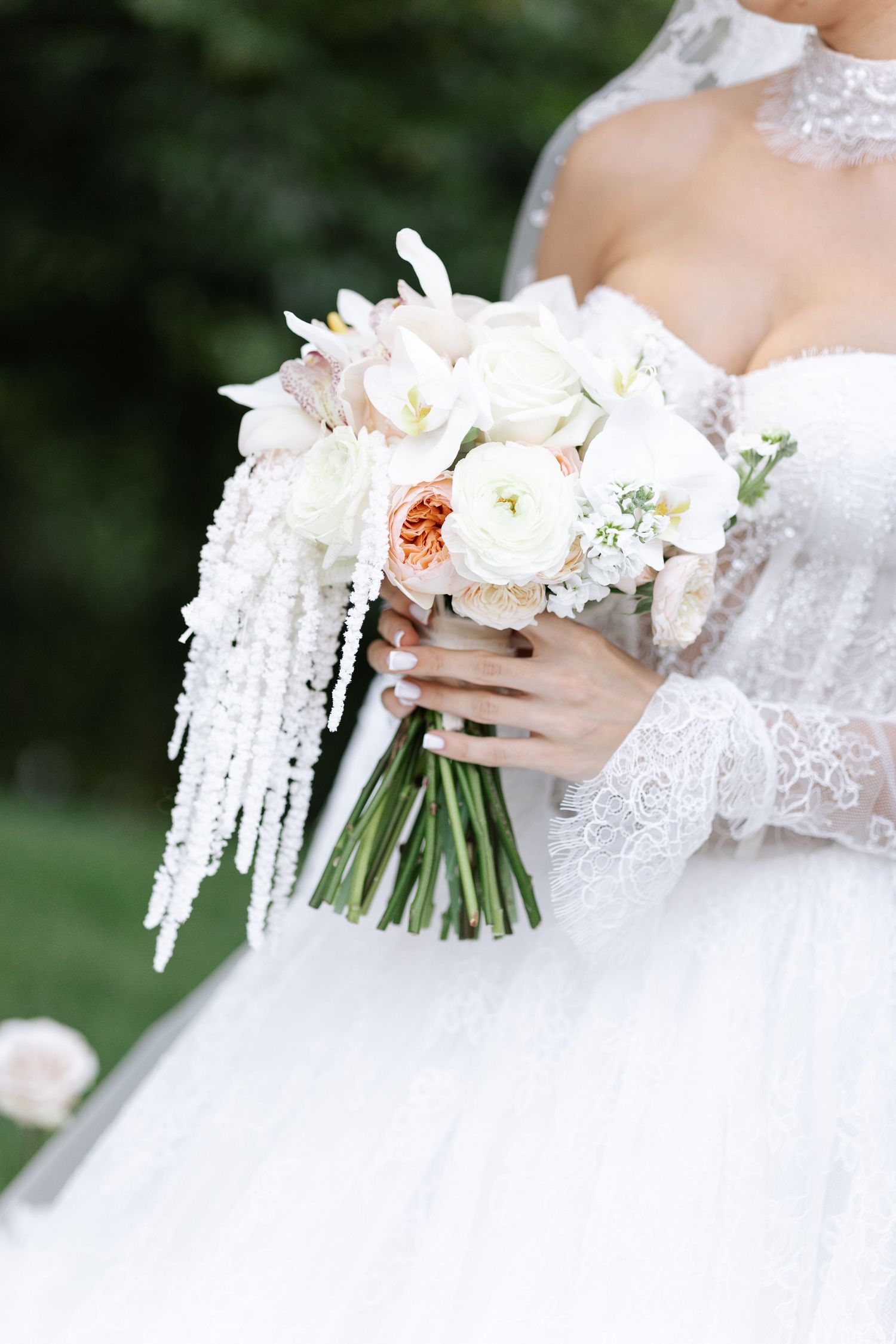 Bridal bouquet with white peonies and cascading elements against a lace wedding dress.