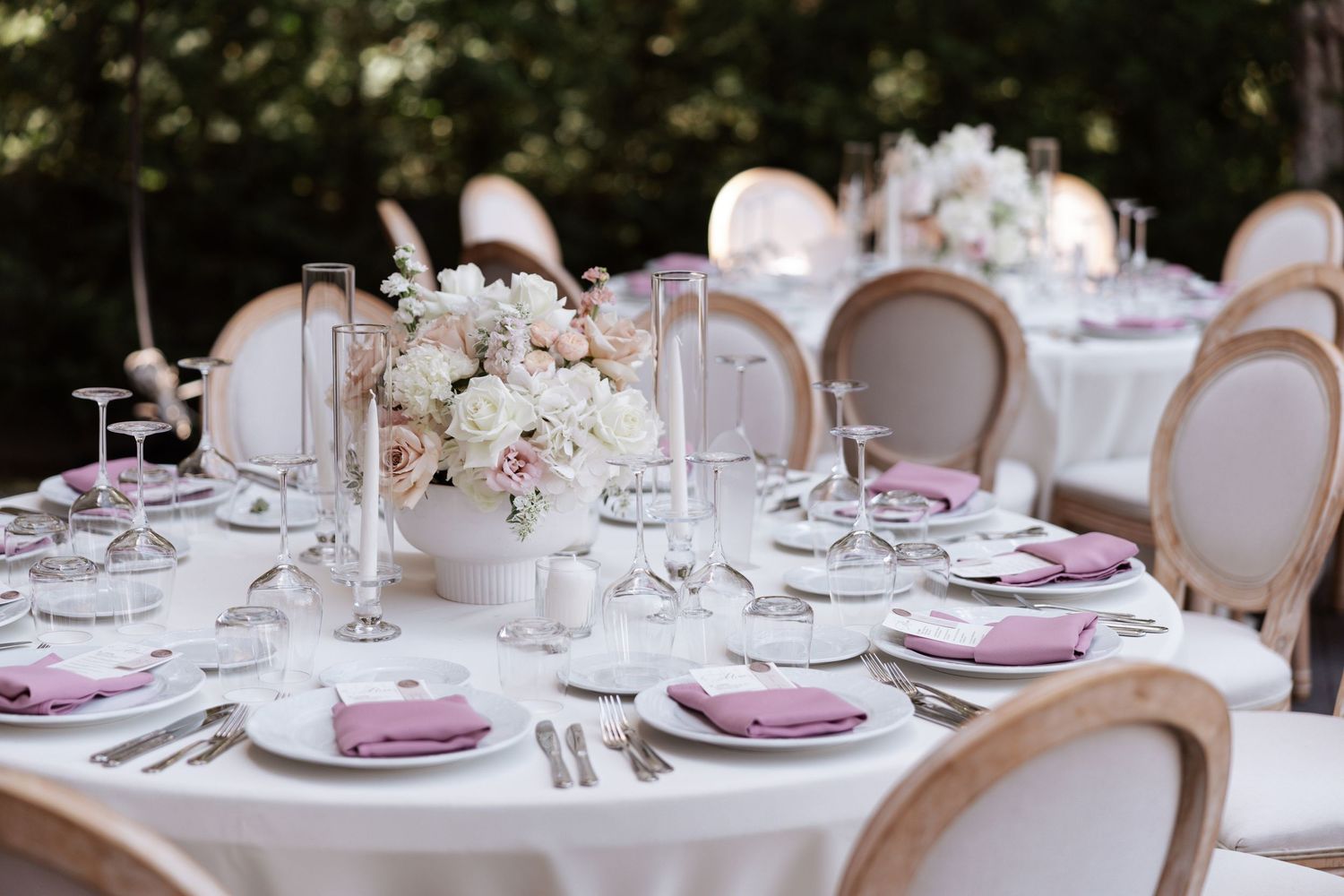 Round reception tables with white linens, mauve napkins and romantic floral centerpieces.