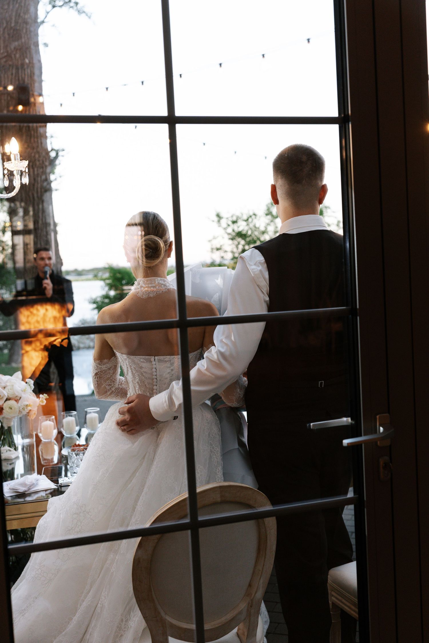 Wedding reception scene through window panes showing formal attire and elegant decor.