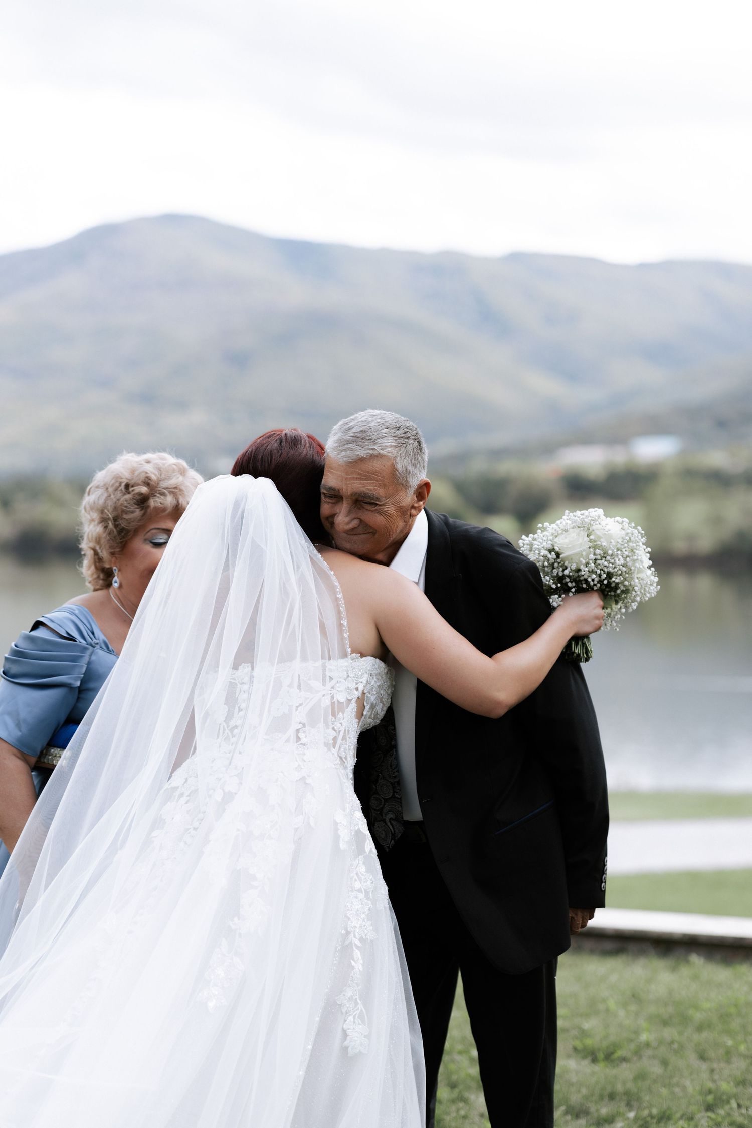 Emotional embrace during an outdoor lakeside wedding ceremony with mountain views.
