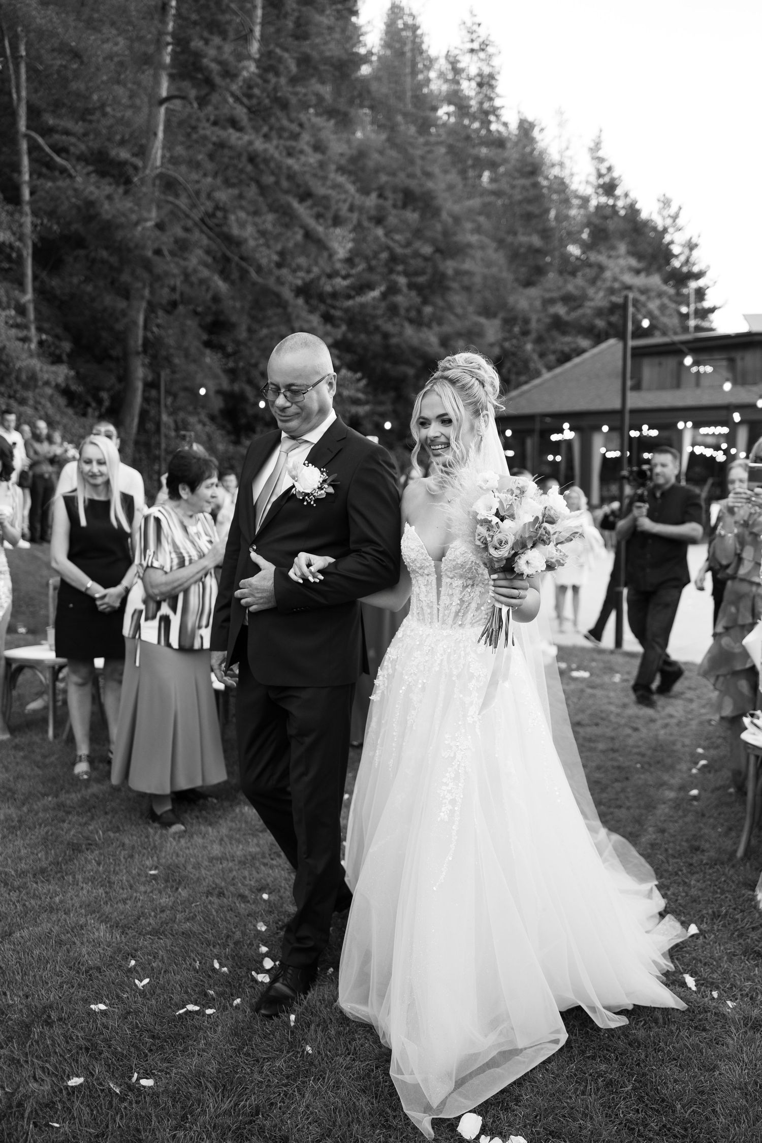 A couple dances together at an outdoor wedding reception surrounded by guests and trees.