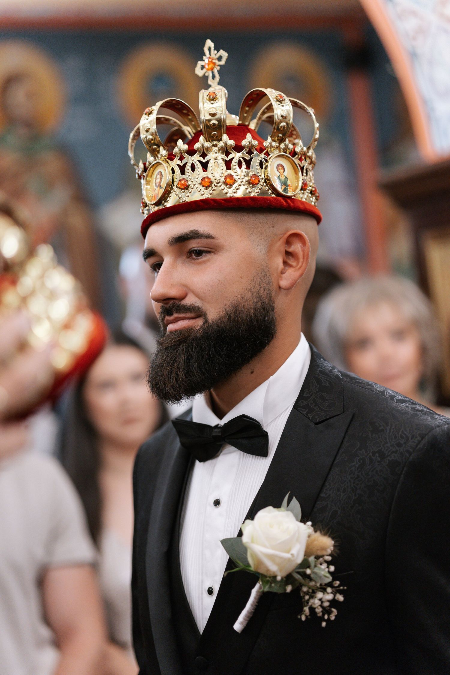 A groom wearing a black tuxedo and gold crown poses during a wedding celebration.