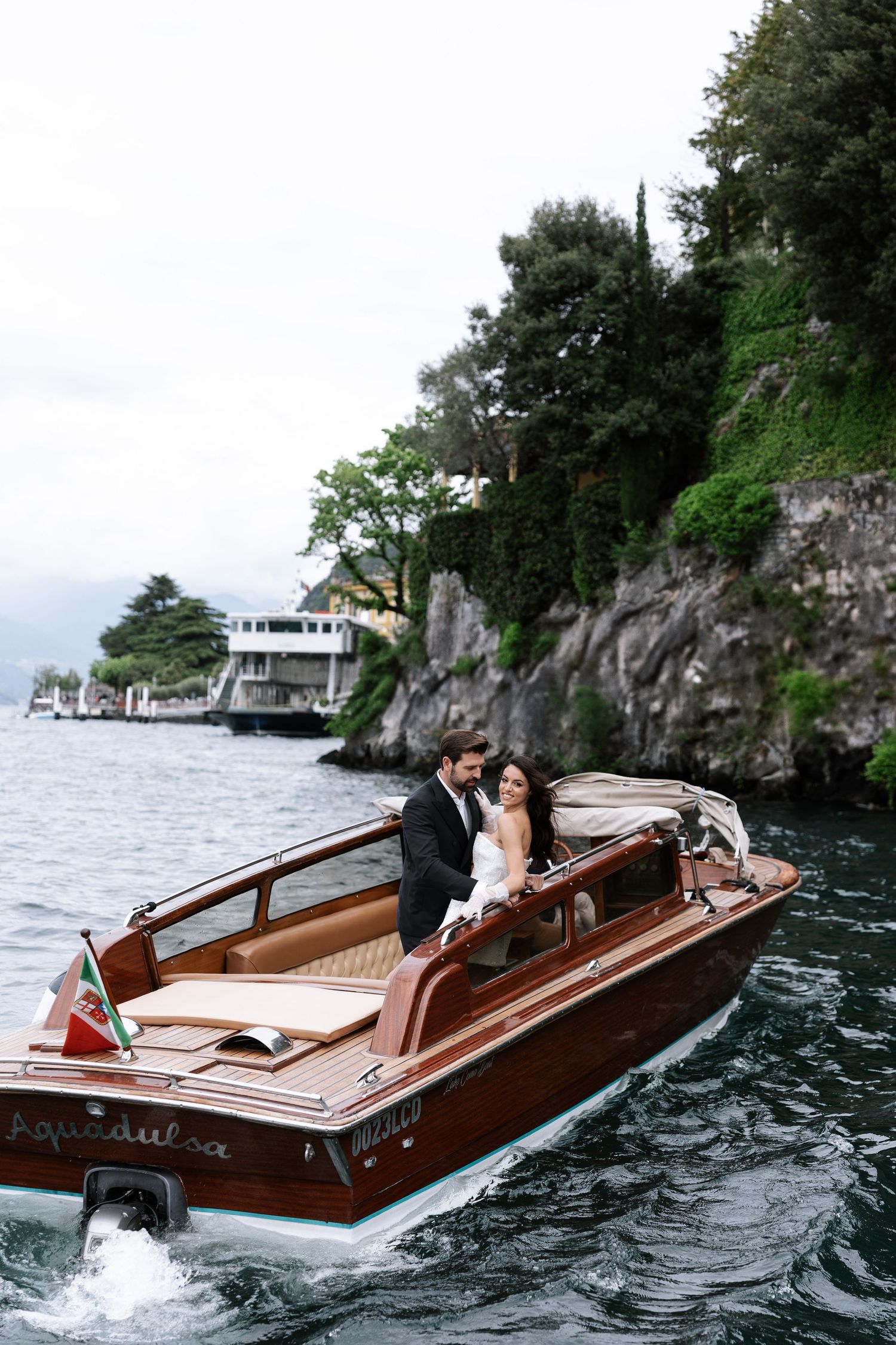 A wooden vintage boat cruises along rocky cliffs on a lake with passengers enjoying a scenic ride.