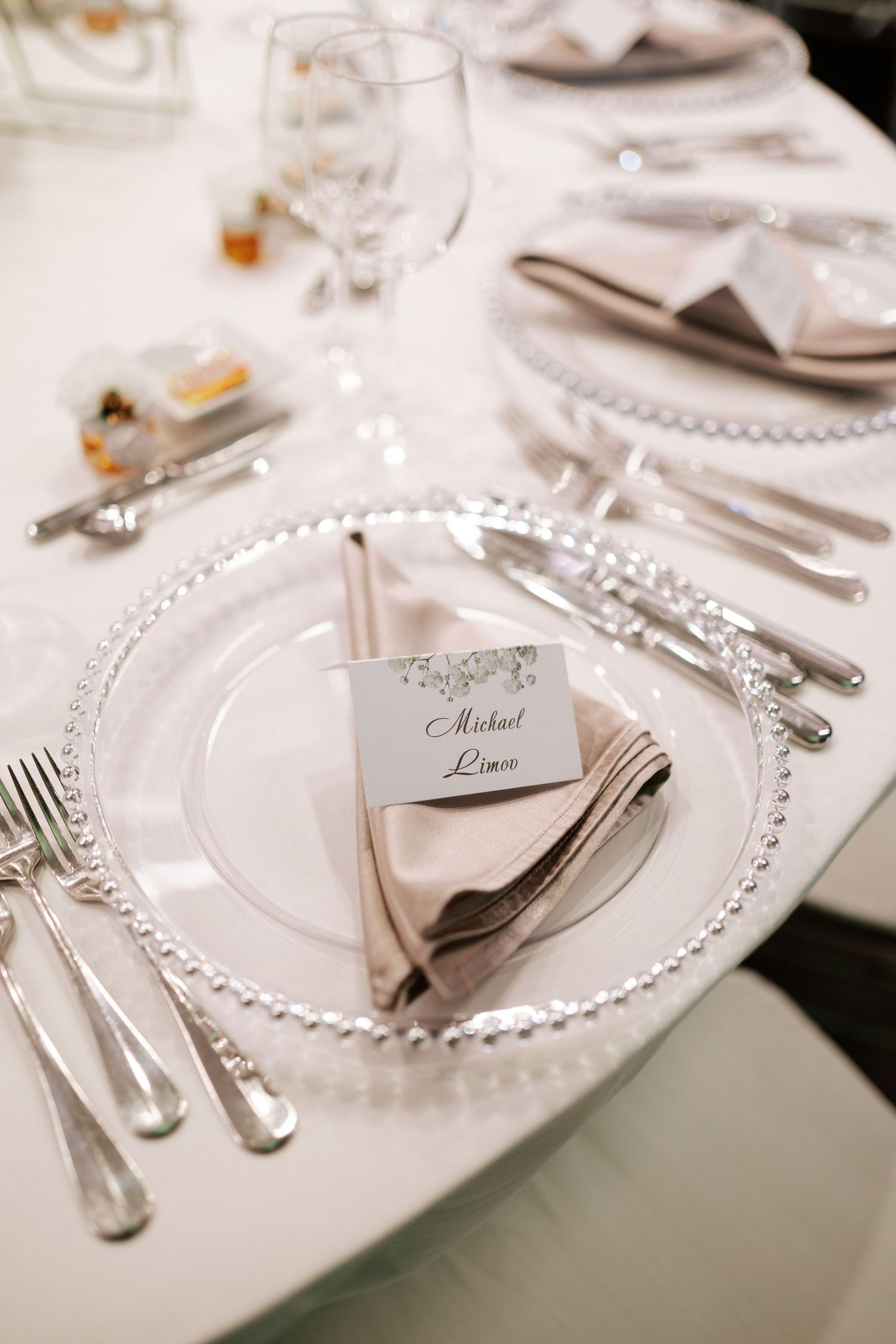 Formal place setting with crystal charger plate, silver cutlery, and personalized name card.