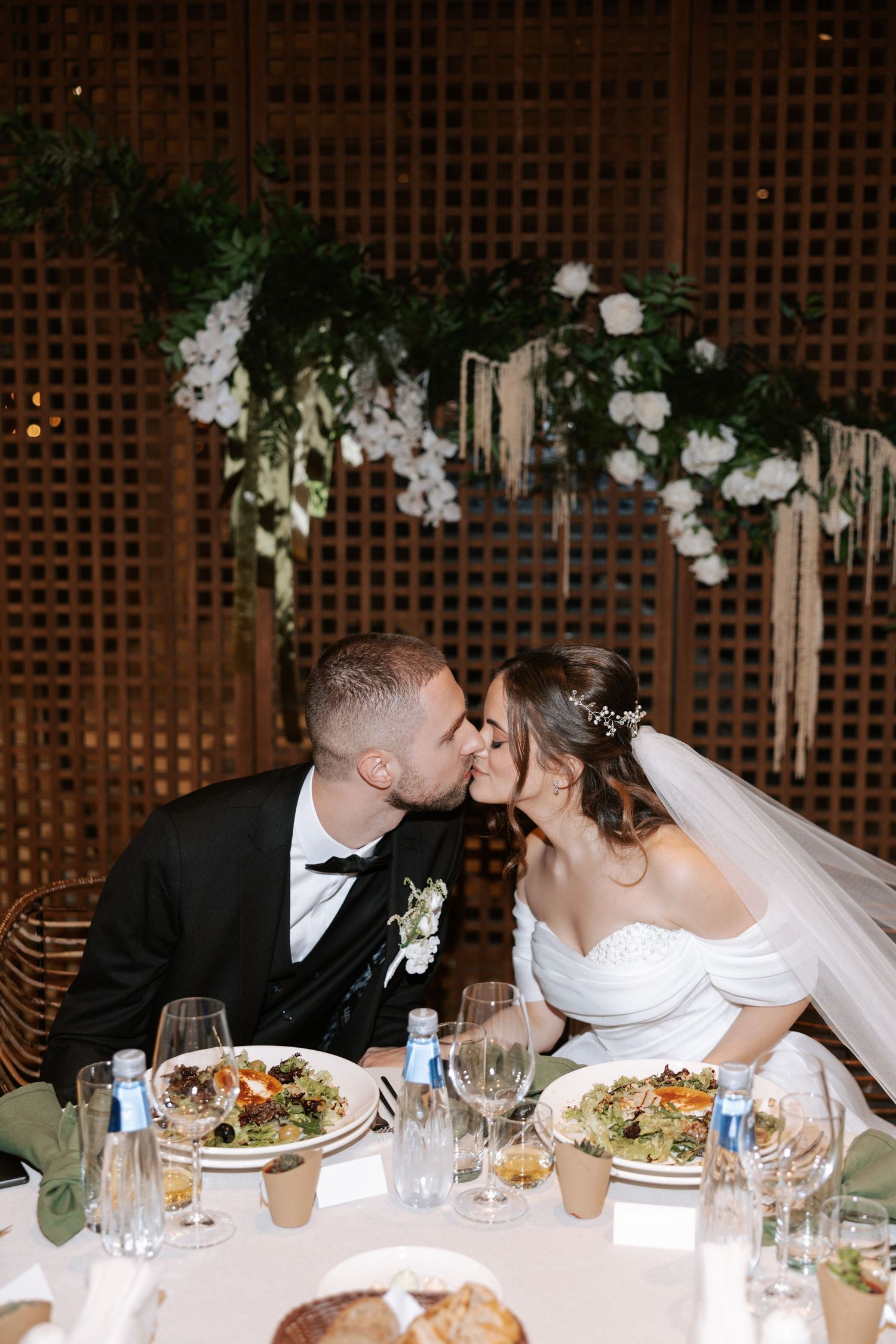 A romantic moment shared between newlyweds at their reception dinner under floral decorations.