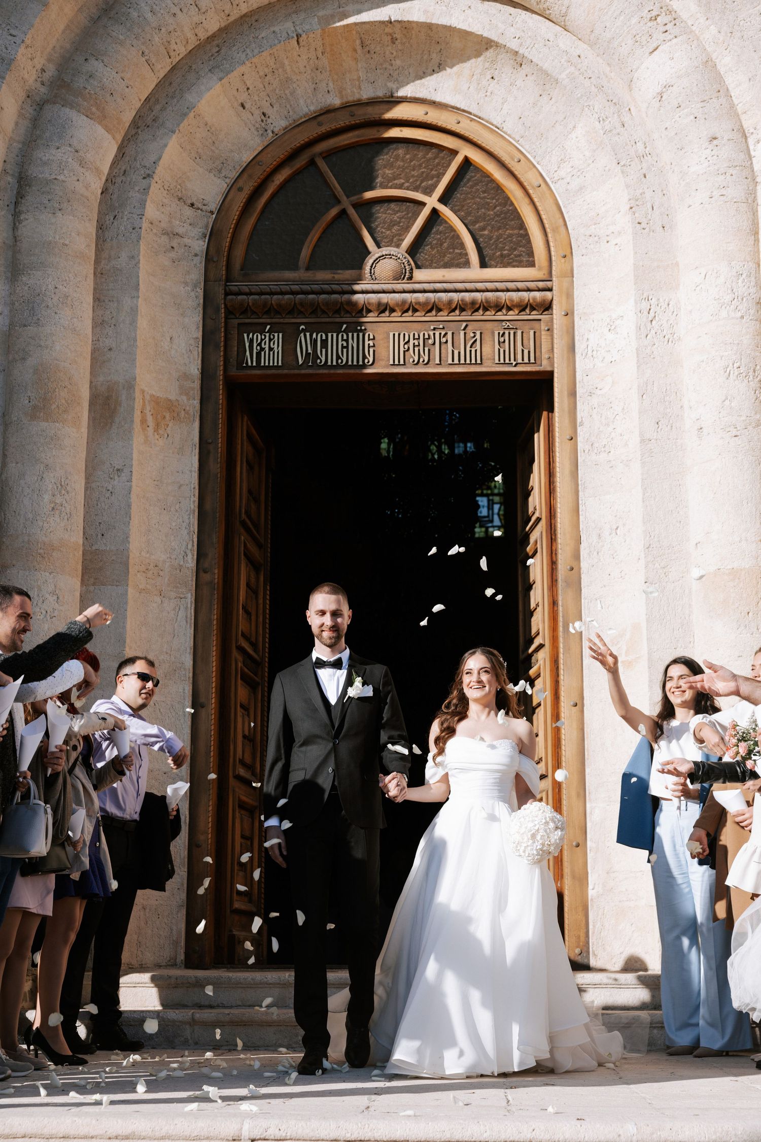 Wedding exit with guests throwing confetti outside a grand stone church entrance.