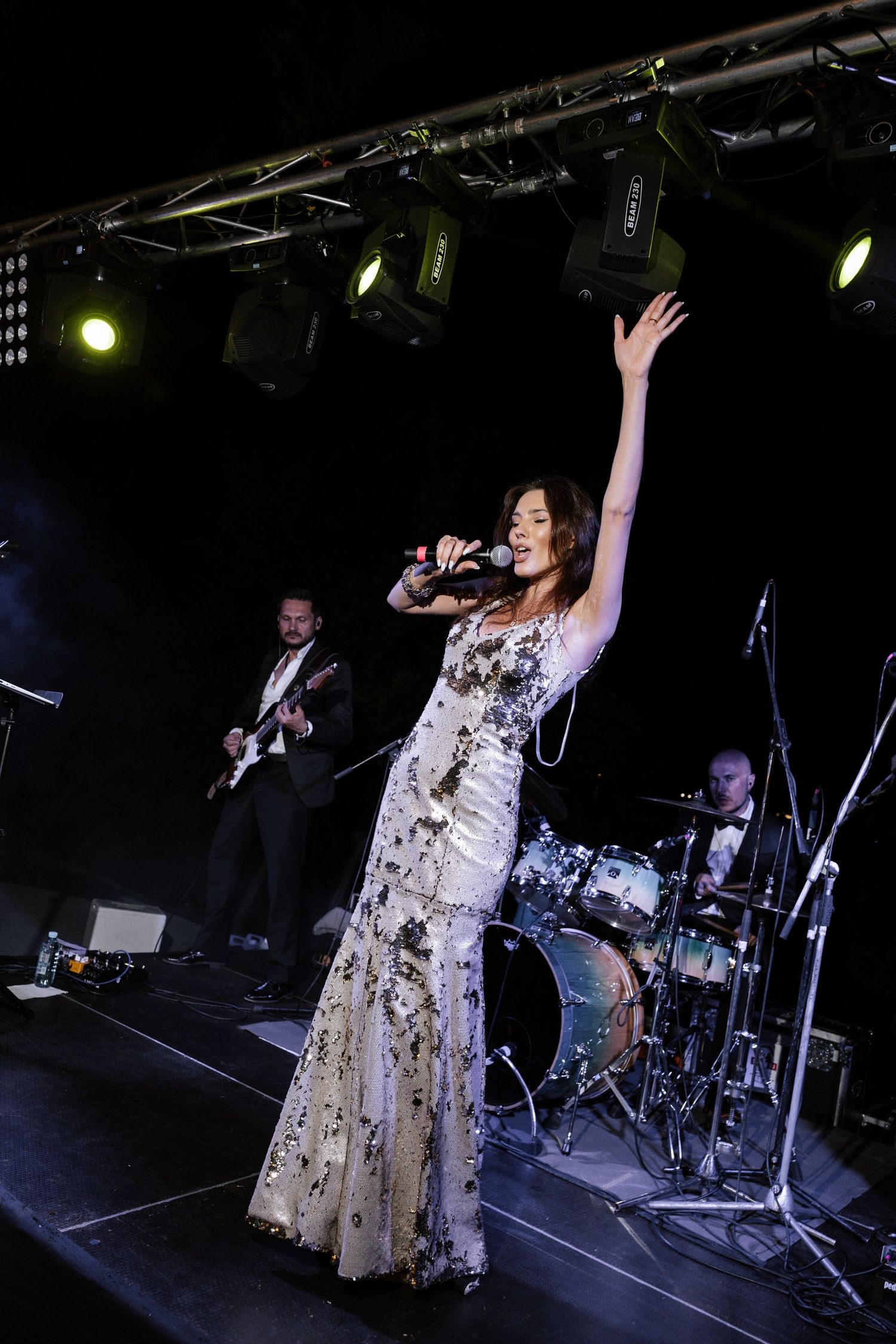 A performer in a sparkly gown sings on stage with a band during a wedding reception.