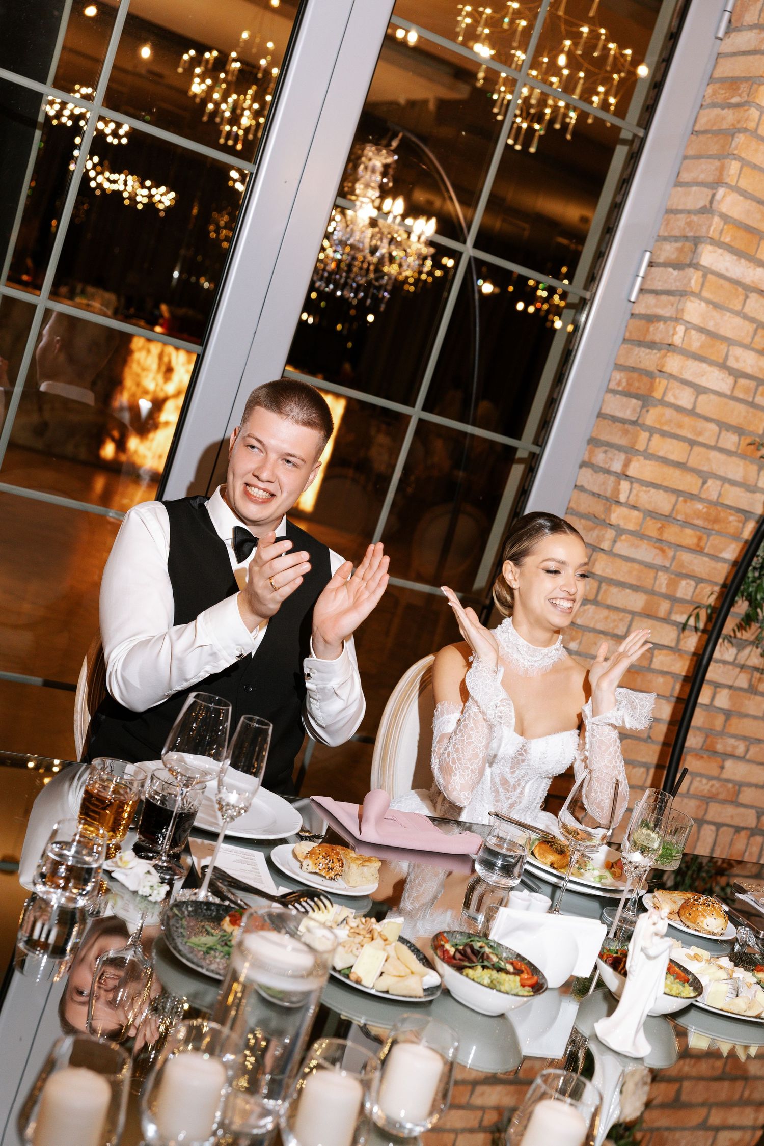 Wedding reception dinner scene with guests dining at decorated tables with warm lighting.