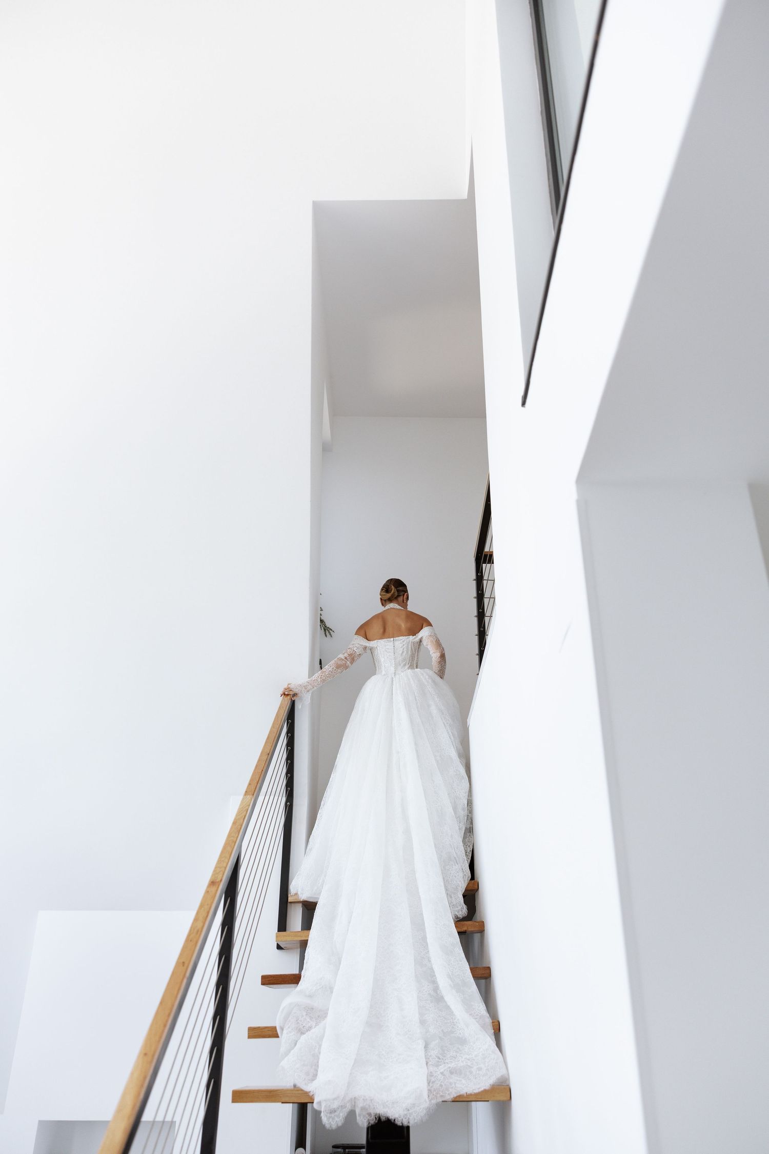 White wedding dress displayed on wooden stairs in a modern minimalist interior.