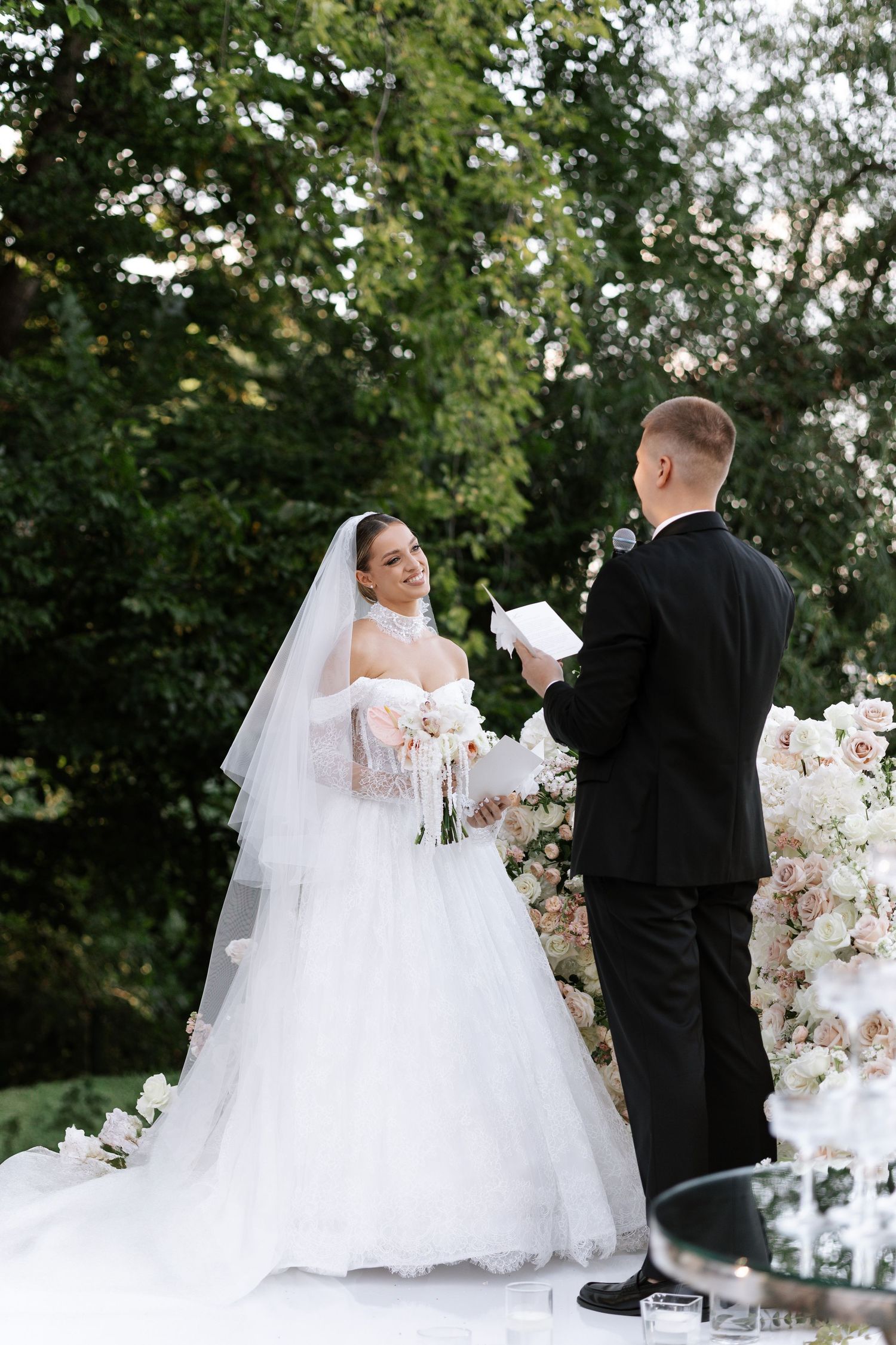 Elegant wedding couple in formal attire sharing a romantic moment outdoors with white floral arrangements.