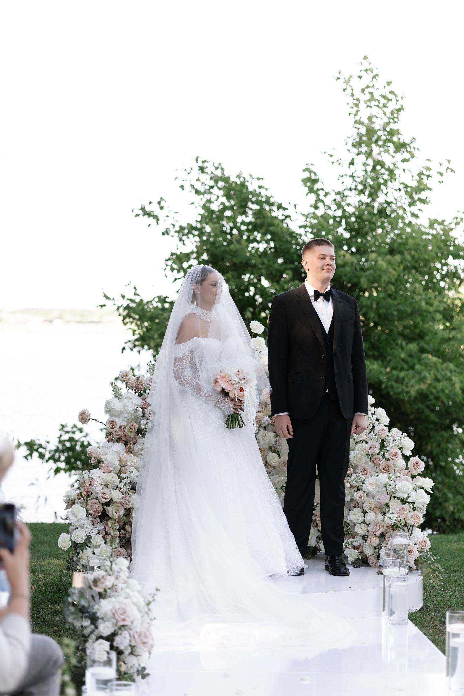 Wedding ceremony setup with floral arch and white decor against a brick building.