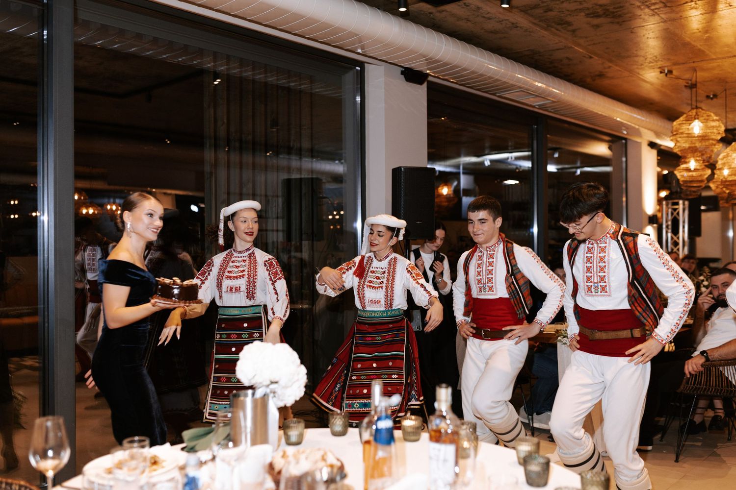 Folk dancers in traditional Eastern European costumes interacting with guests at a wedding reception.
