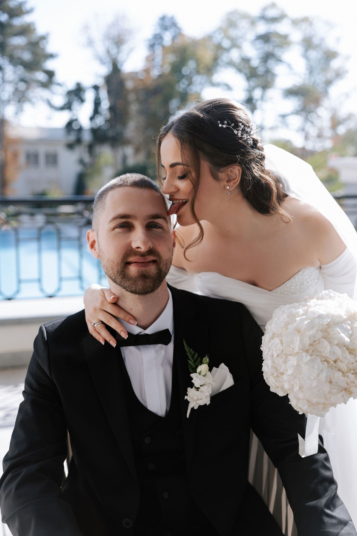 Intimate moment between newlyweds on balcony with ornate railing and pool view.