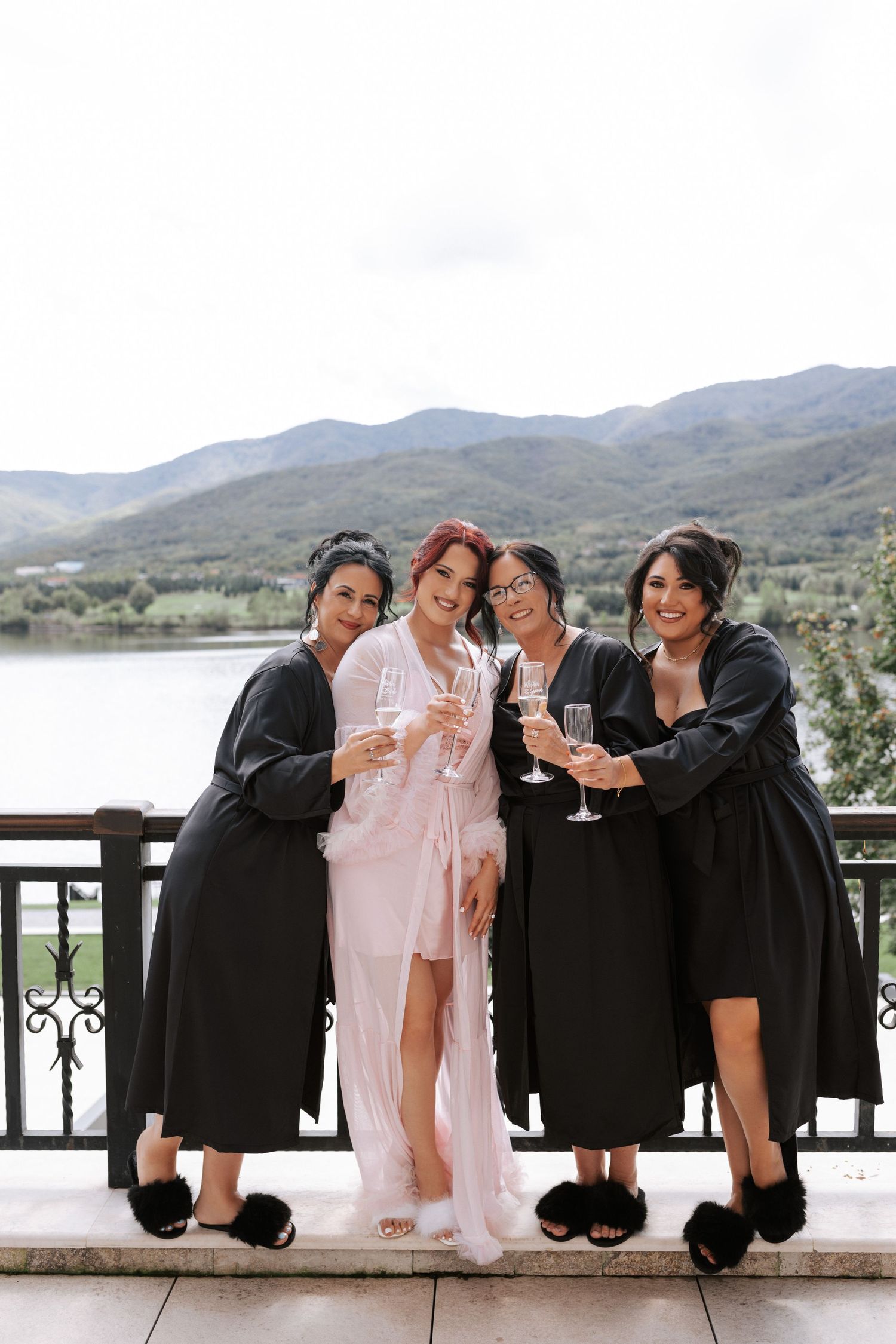 Four people in robes holding champagne glasses on mountain view balcony.