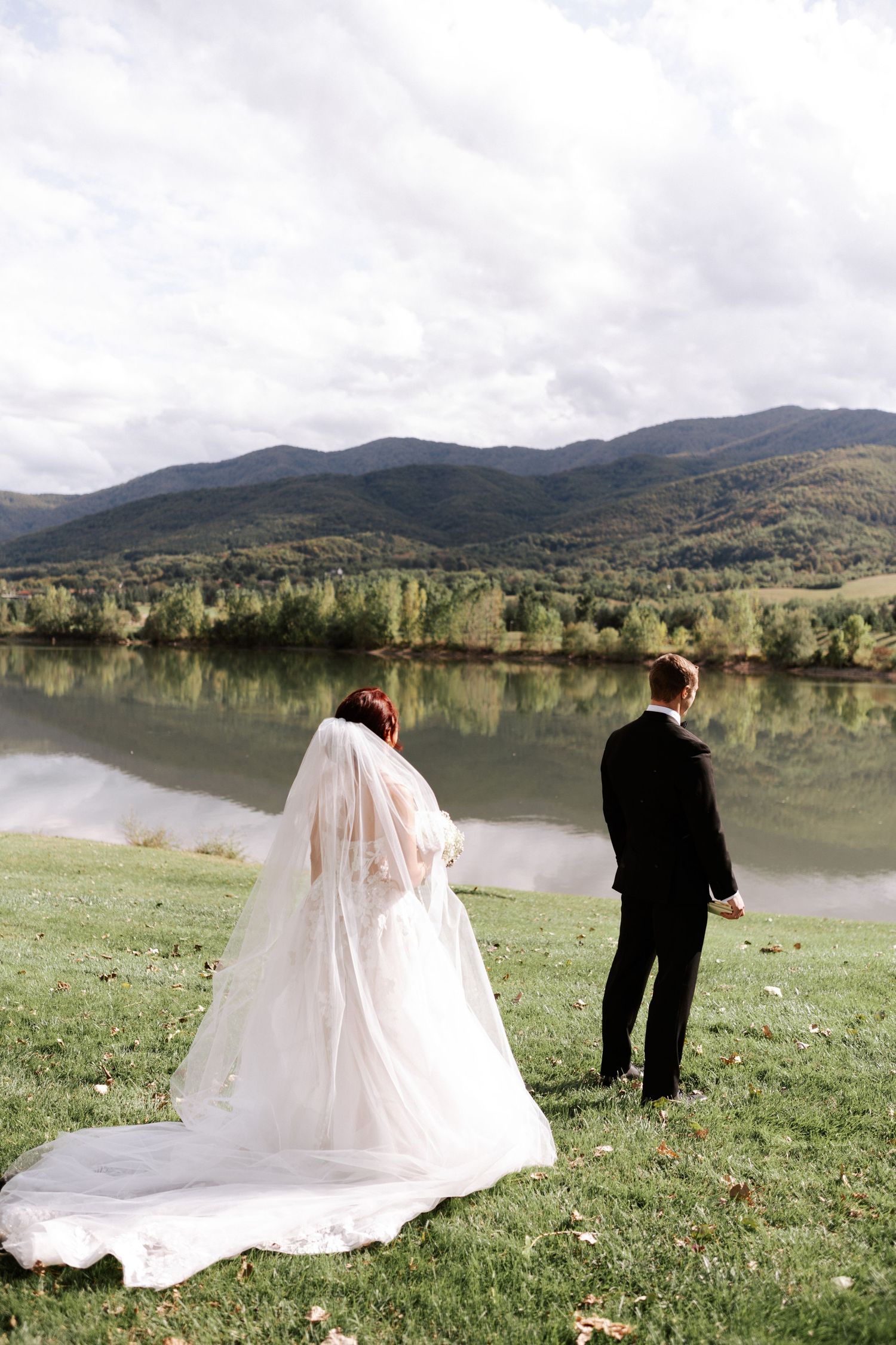 Bride and groom standing on hillside overlooking a serene mountain lake.