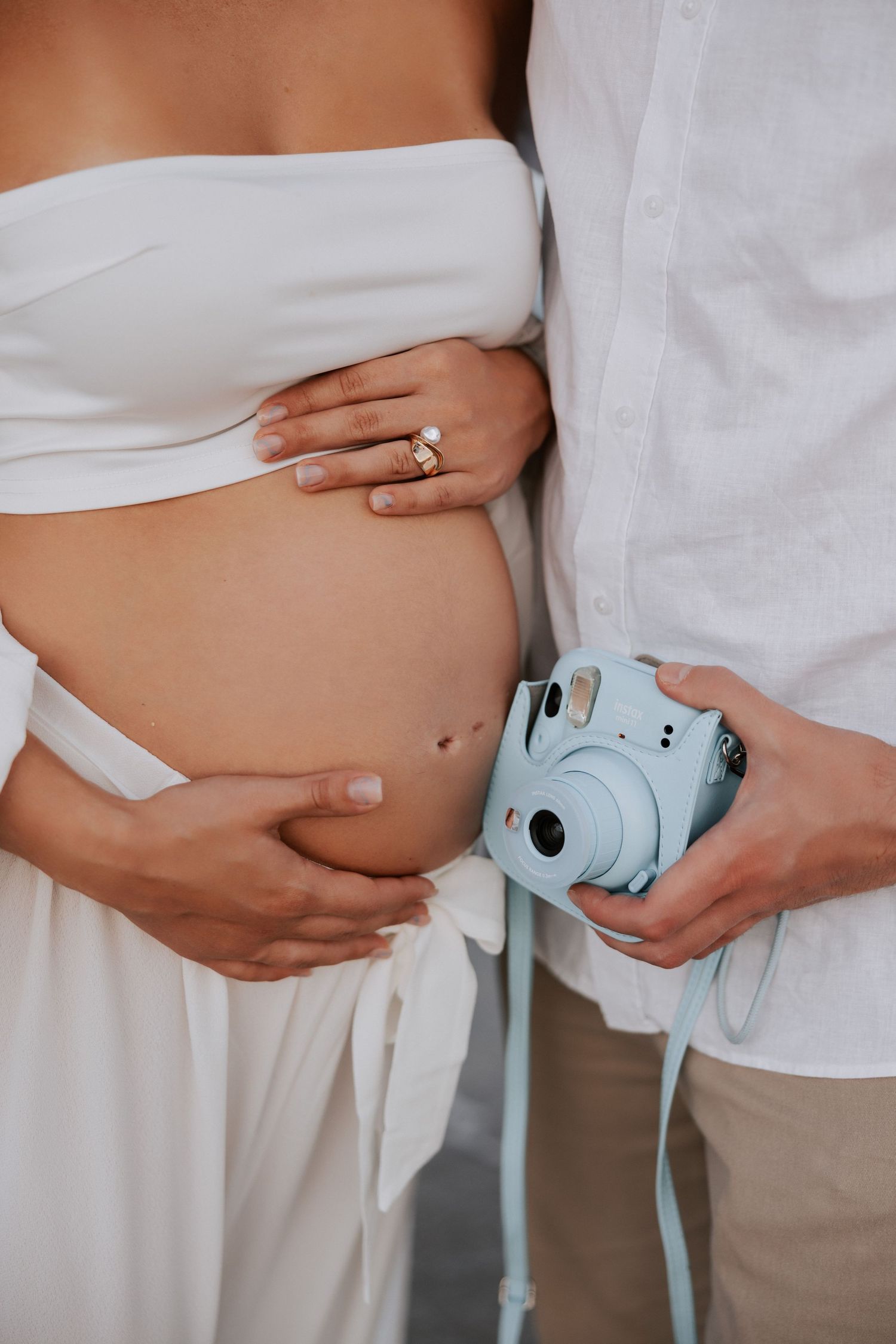 Close-up of a pregnant belly with hands holding a blue instant camera.