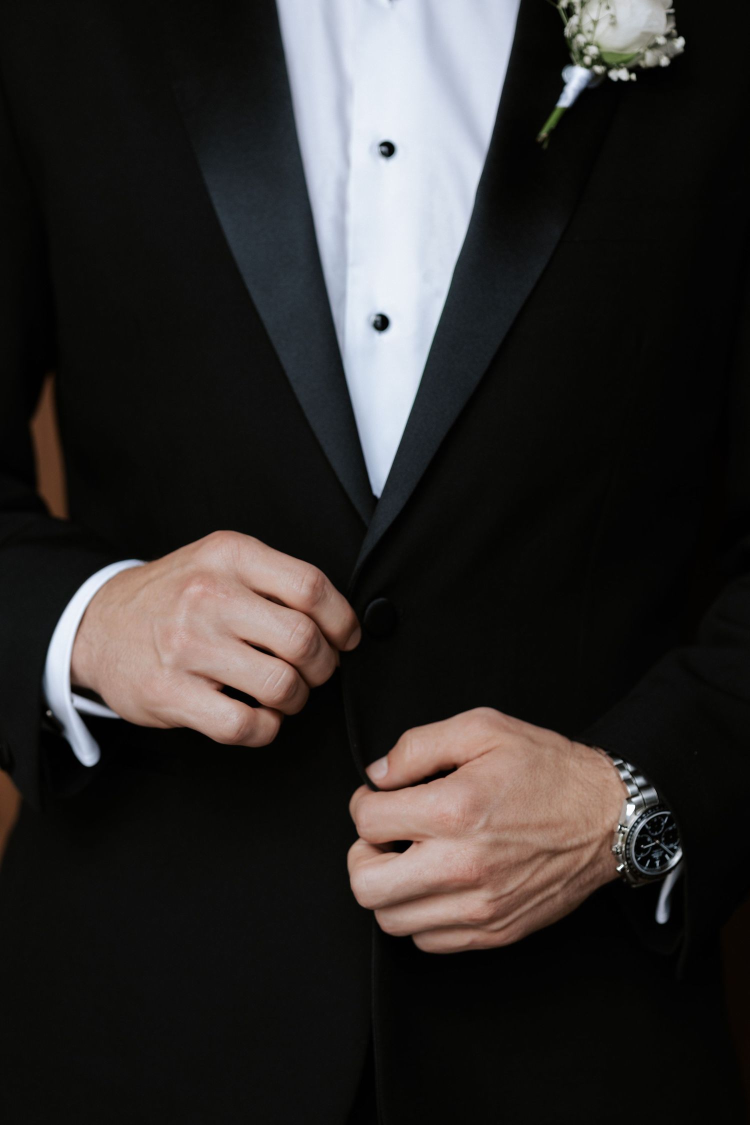 Close-up detail of groom's classic black tuxedo with white boutonniere.