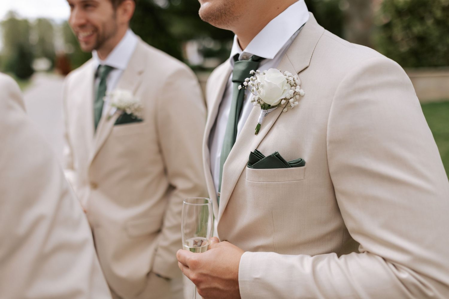 Detail shot of cream suit jackets with boutonnières and sage green ties.