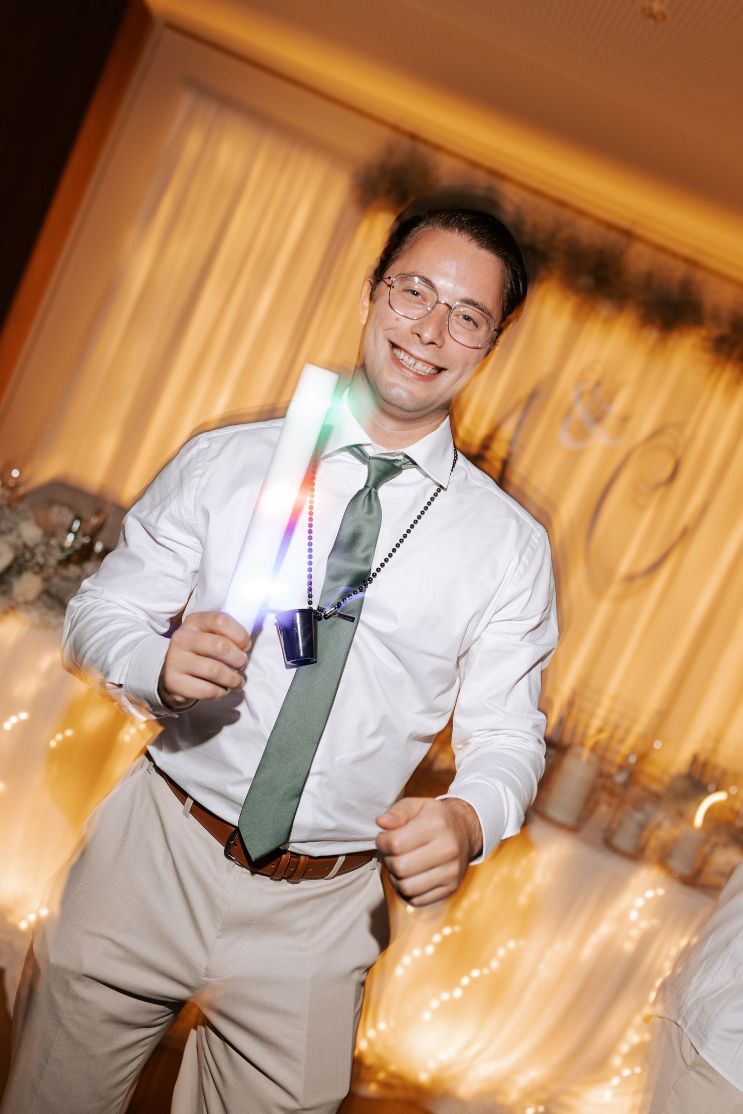 Guest in white shirt and green tie smiles while holding a light-up party favor.