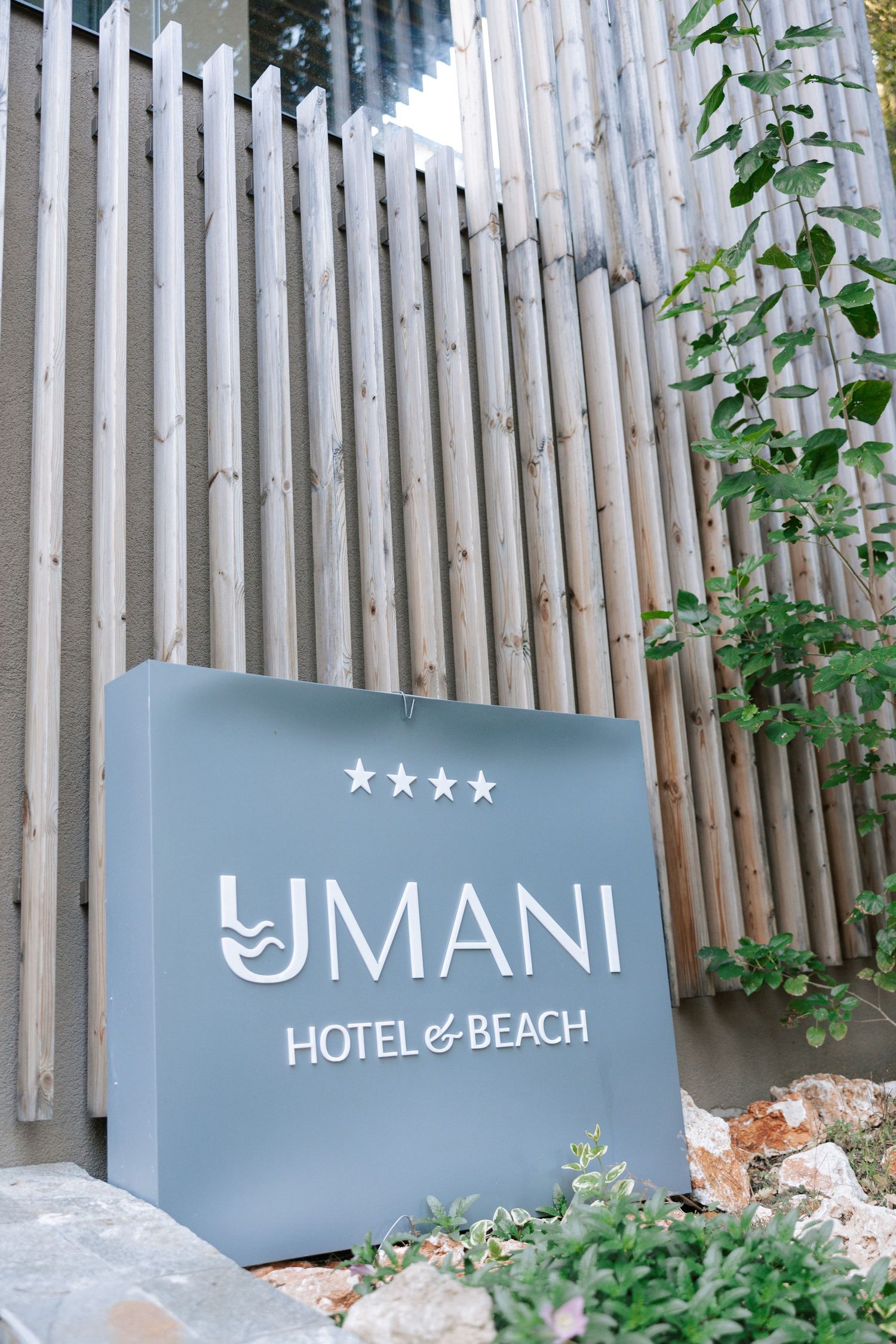 An entrance sign for the four-star Umani Hotel & Beach with wooden slat backdrop.
