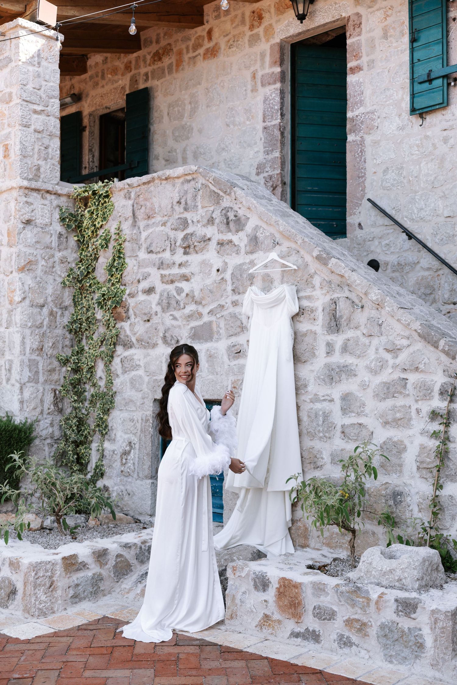 White ghost decorations stand against a rustic stone wall with green shutters and climbing vines.
