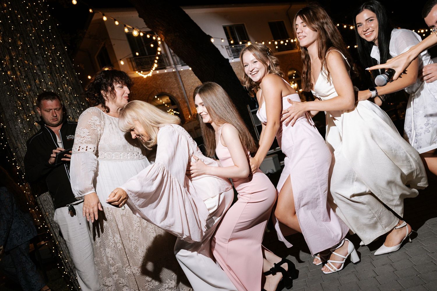 Wedding party dances in formal attire under string lights at night.