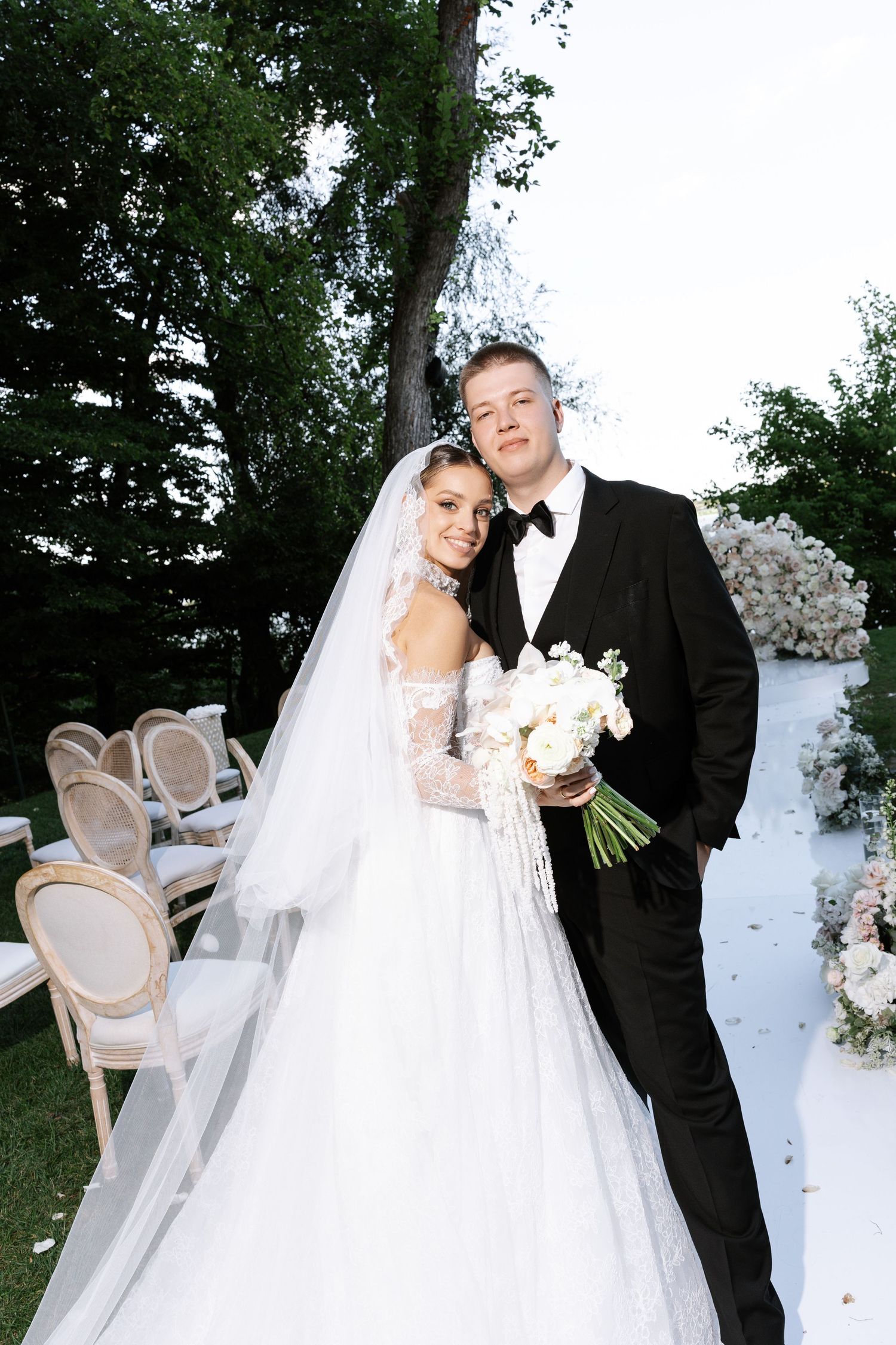 A romantic wedding portrait featuring elegant white decor and floral arrangements in an outdoor garden setting.