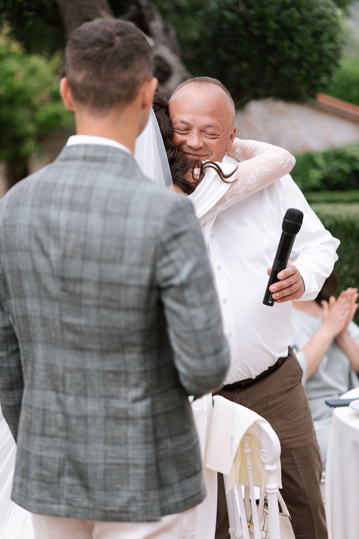 Wedding guests share emotional embraces during an outdoor reception celebration in a garden setting.