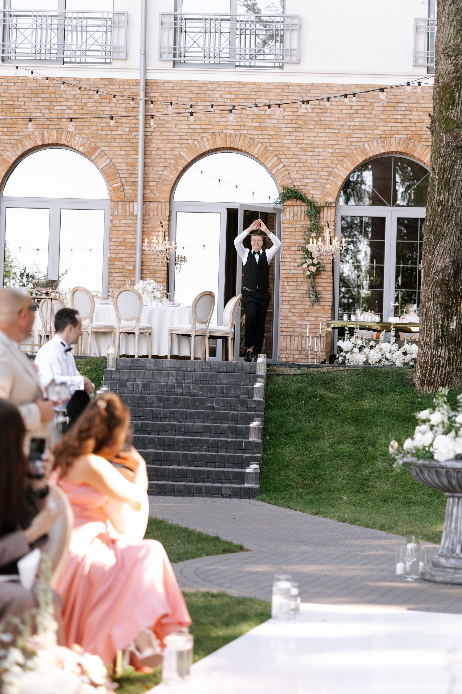 Wedding ceremony setup with white chairs and brick building backdrop featuring elegant stone steps and arches.