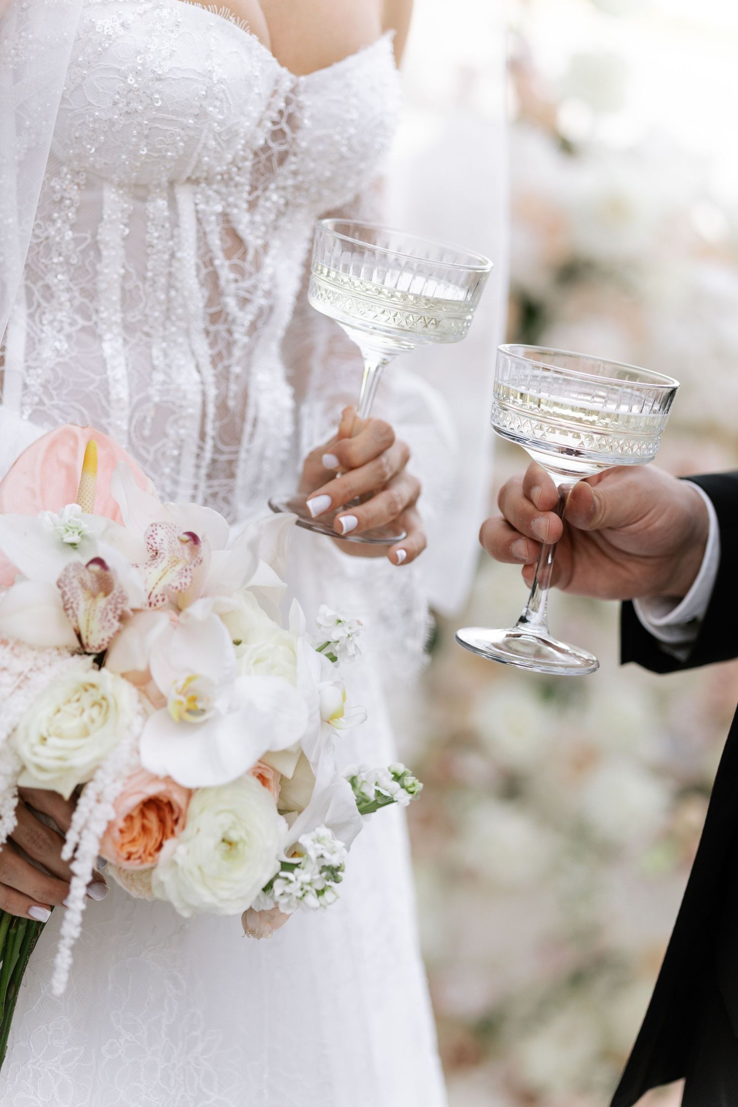 Close-up of champagne toast with bridal bouquet featuring white and pink roses.