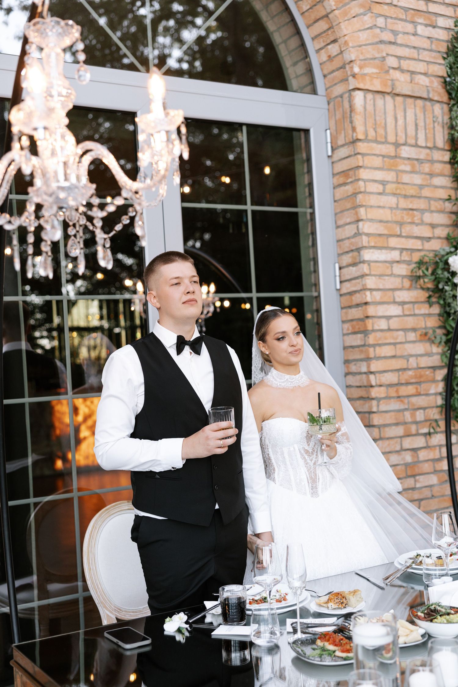 Wedding reception guests in formal attire enjoying dinner under crystal chandeliers.