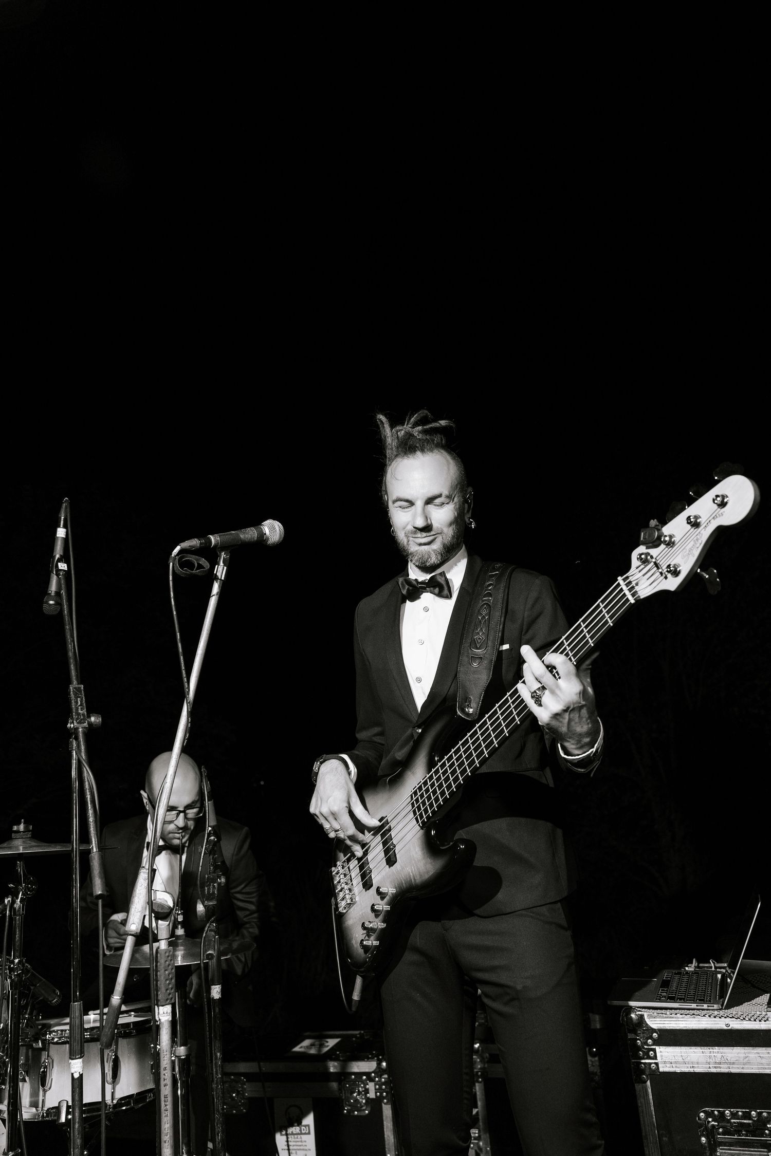 Bass player in tuxedo performs on stage at formal event in black and white.