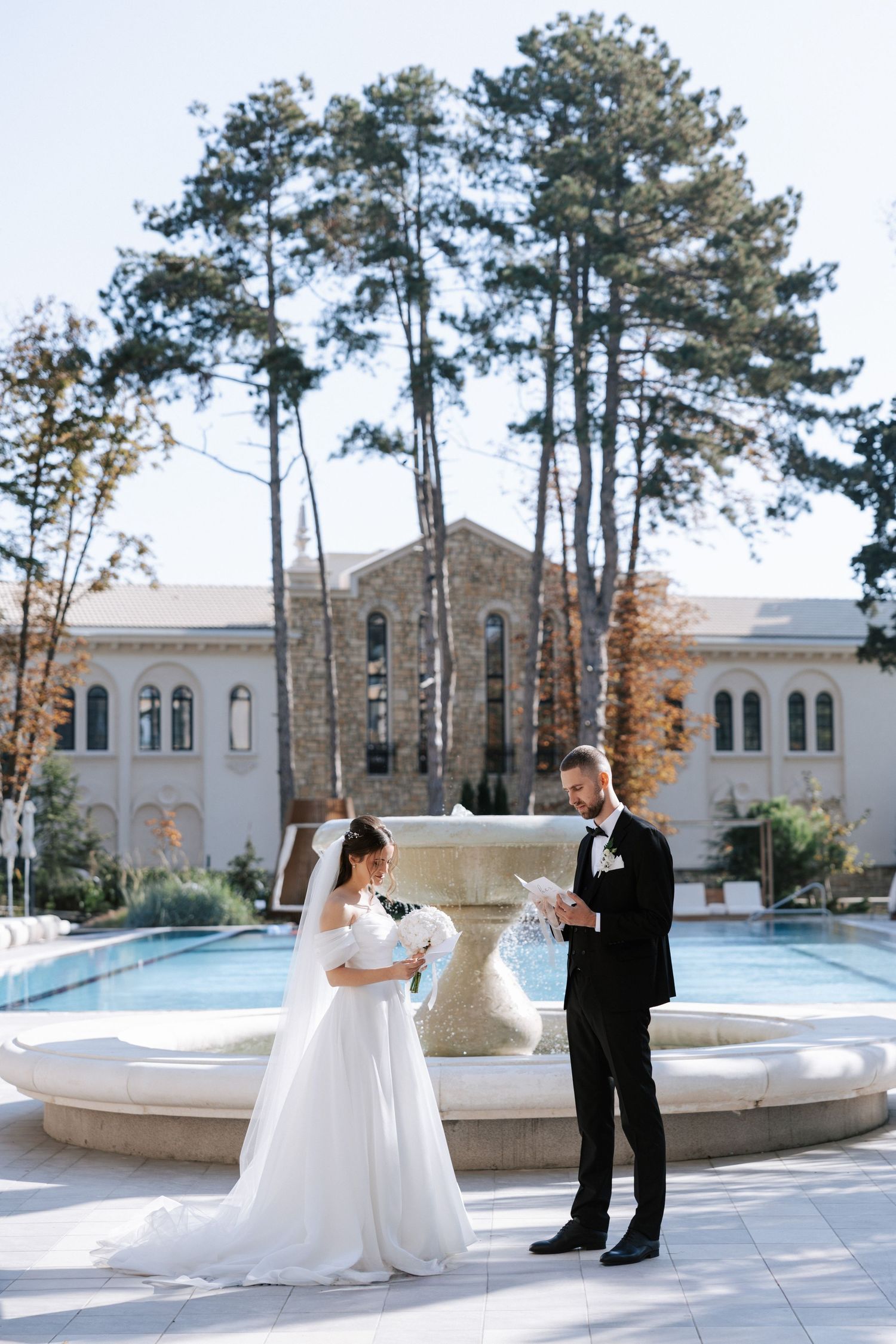 Wedding couple reading vows in front of an elegant stone fountain and mansion.