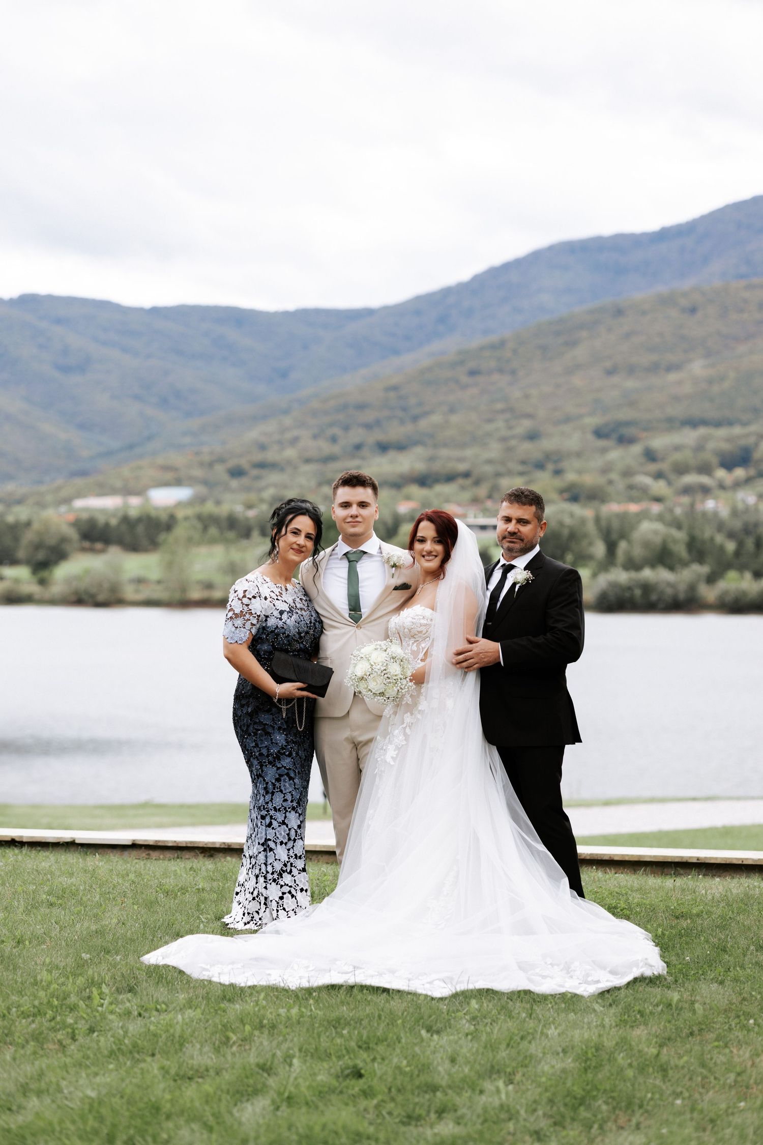 Wedding party poses for formal photo with mountain lake scenery in background.
