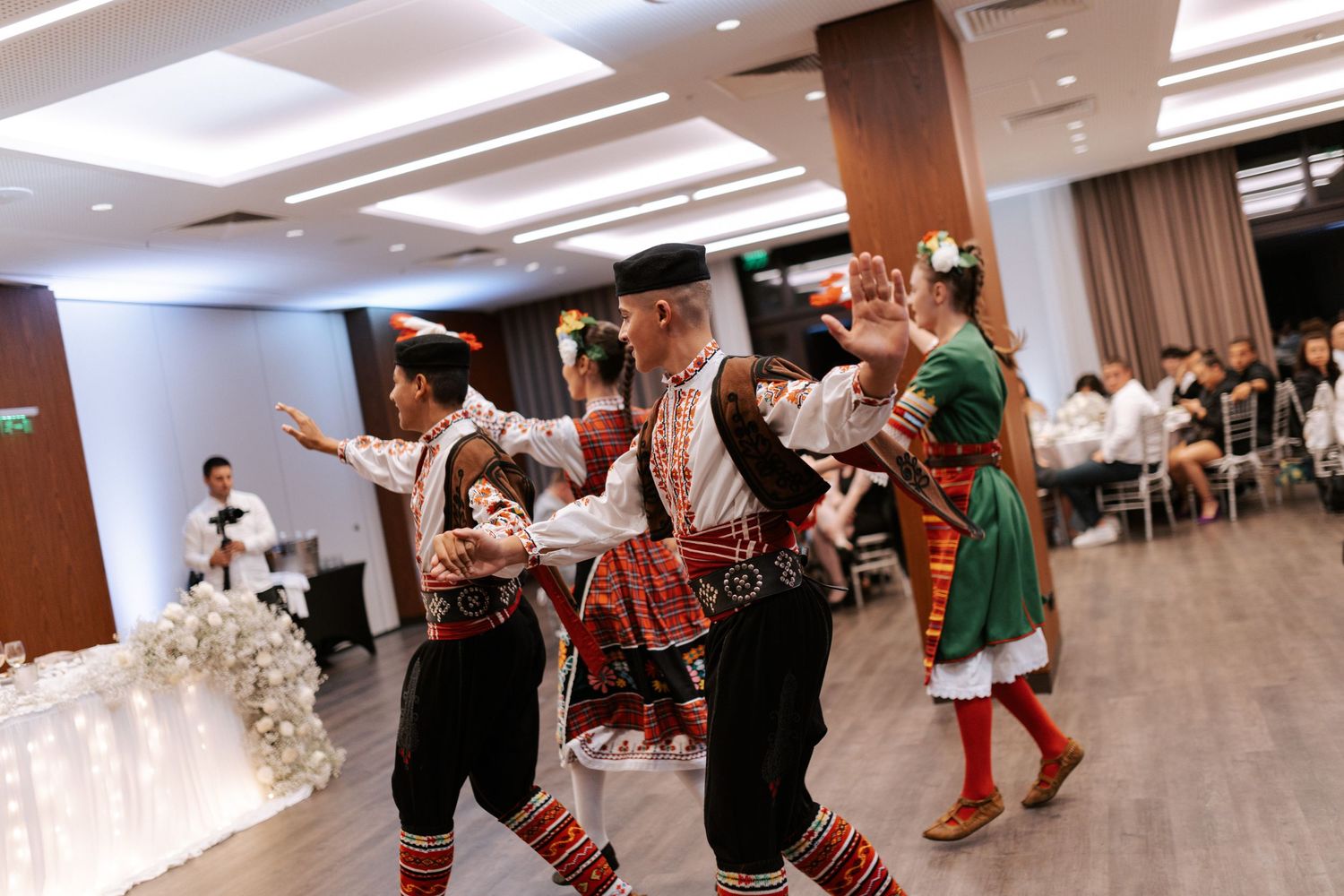 Traditional folk dancers perform in colorful costumes during a wedding reception celebration.