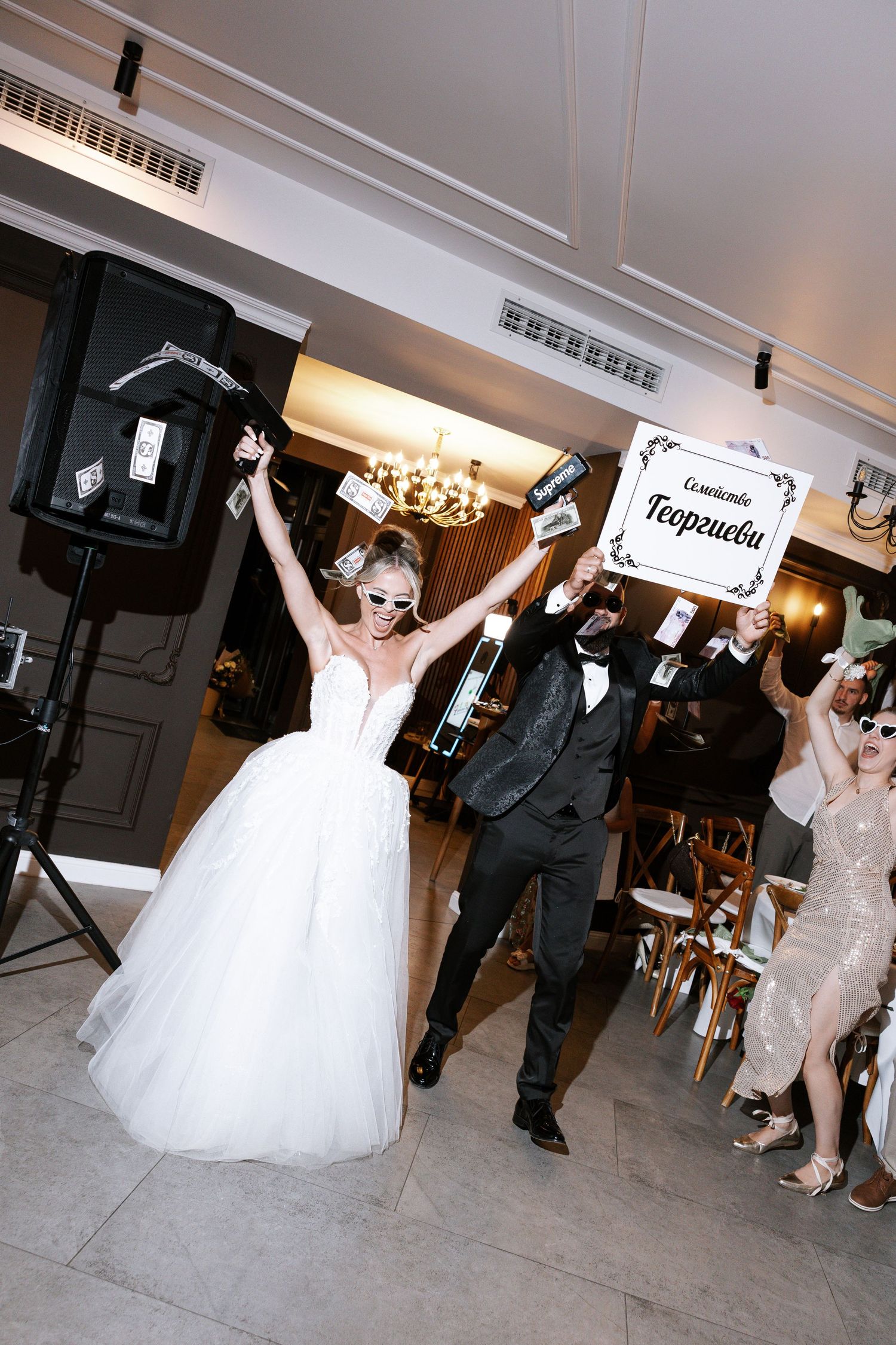 Wedding reception guests dance and celebrate with raised signs on the dance floor at an indoor venue.