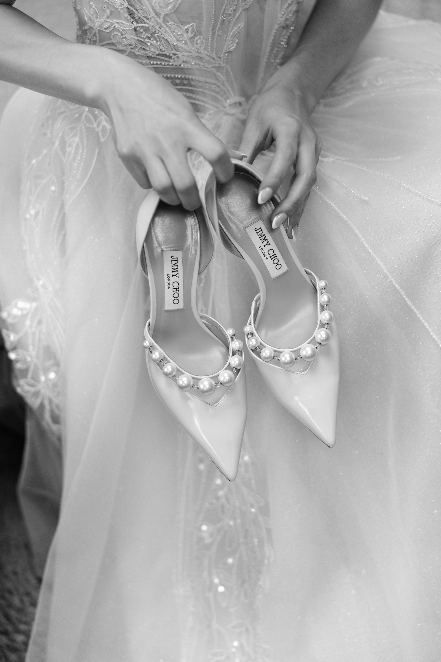 A series of hands adjusting delicate pearl bracelets on white tulle fabric in a wedding preparation setting.