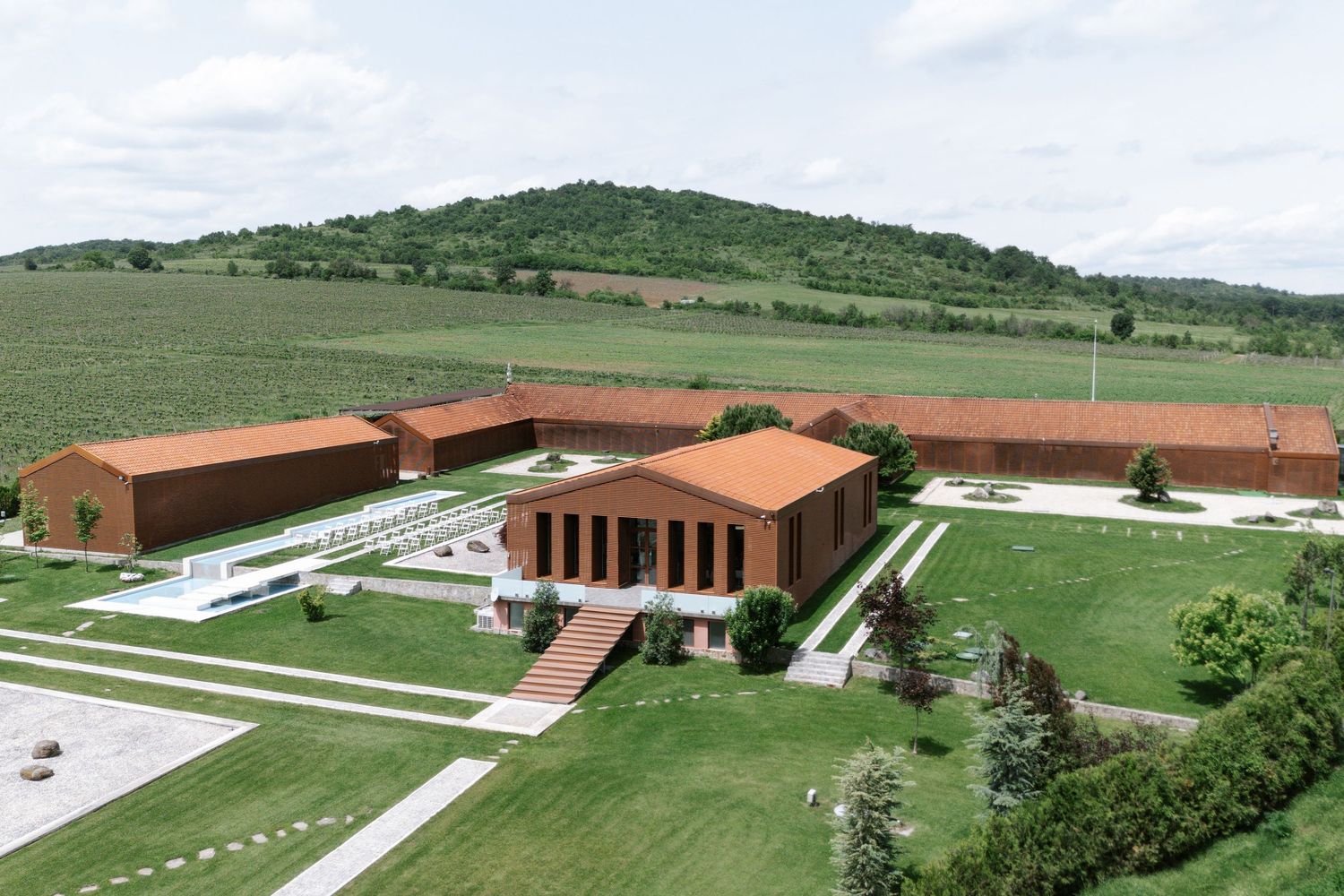 Modern brick school building complex surrounded by green landscaping and sports fields viewed from an aerial perspective.