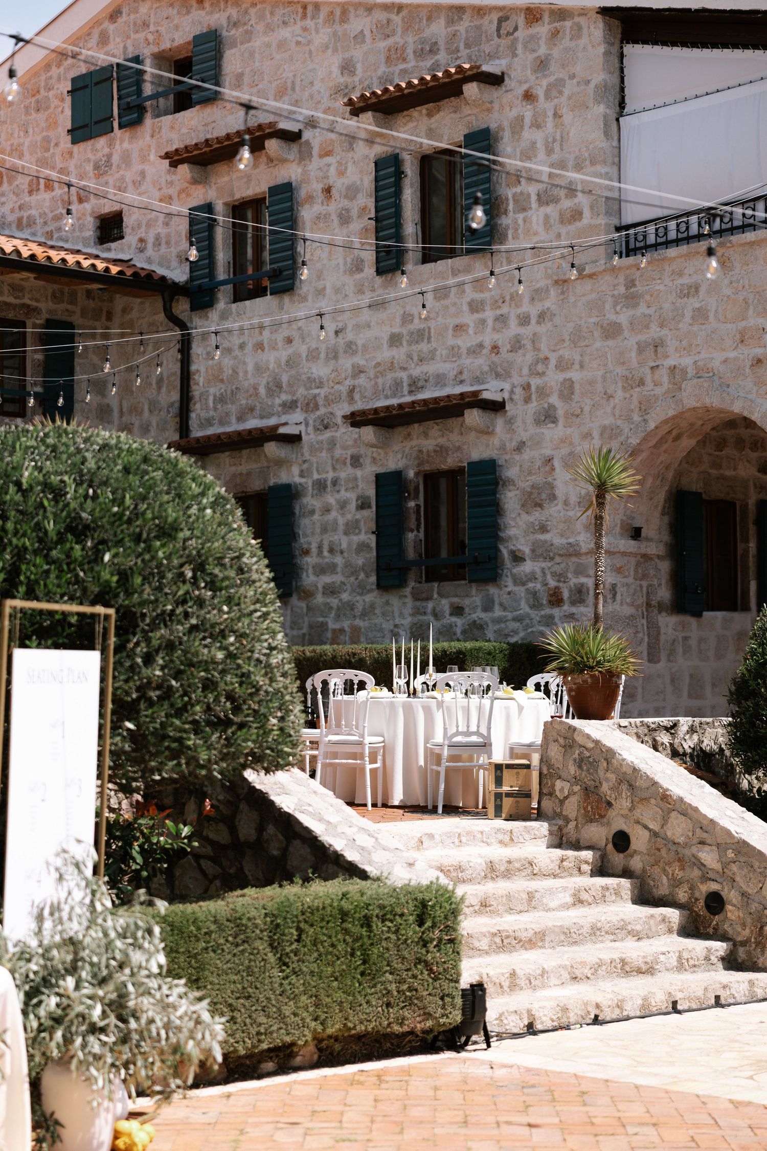 Stone villa terrace with white outdoor furniture and Mediterranean landscaping features curved steps and terra cotta tiles.