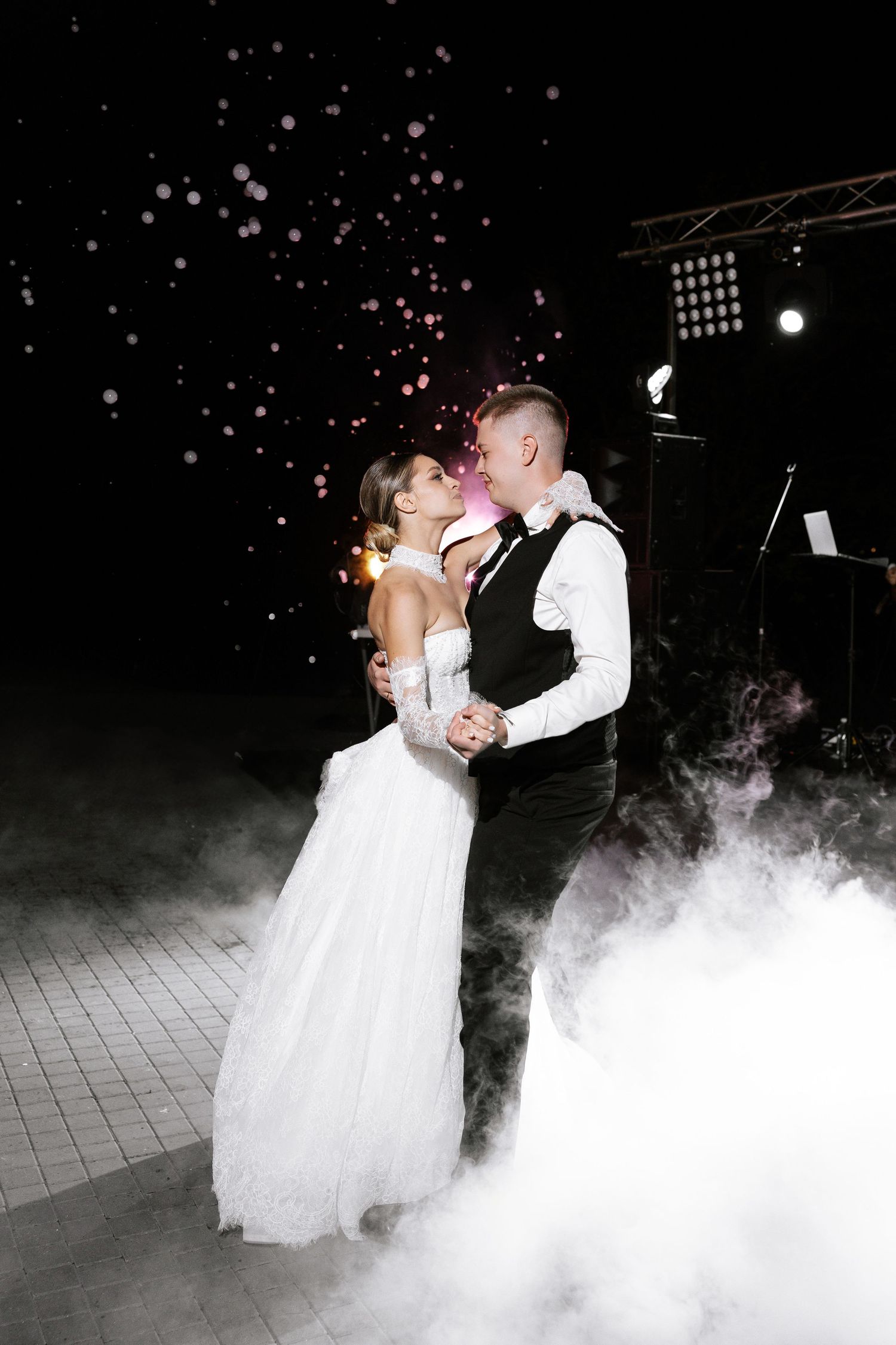 A couple dances in a cloud of fog on a dark dance floor with sparkling lights above.