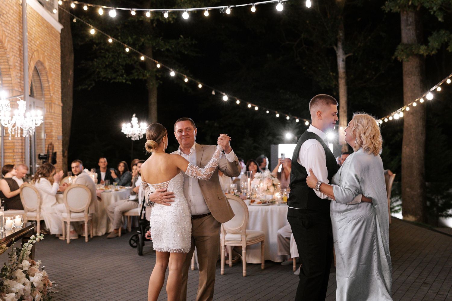 Outdoor wedding reception with string lights and guests dancing under the night sky.