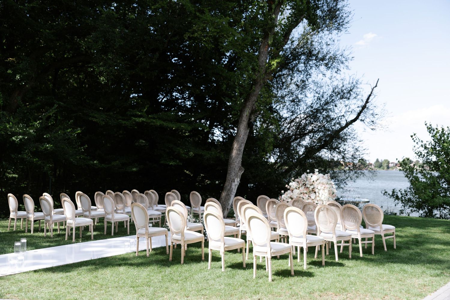 White chairs arranged for an outdoor wedding ceremony on a lawn overlooking a waterfront view.