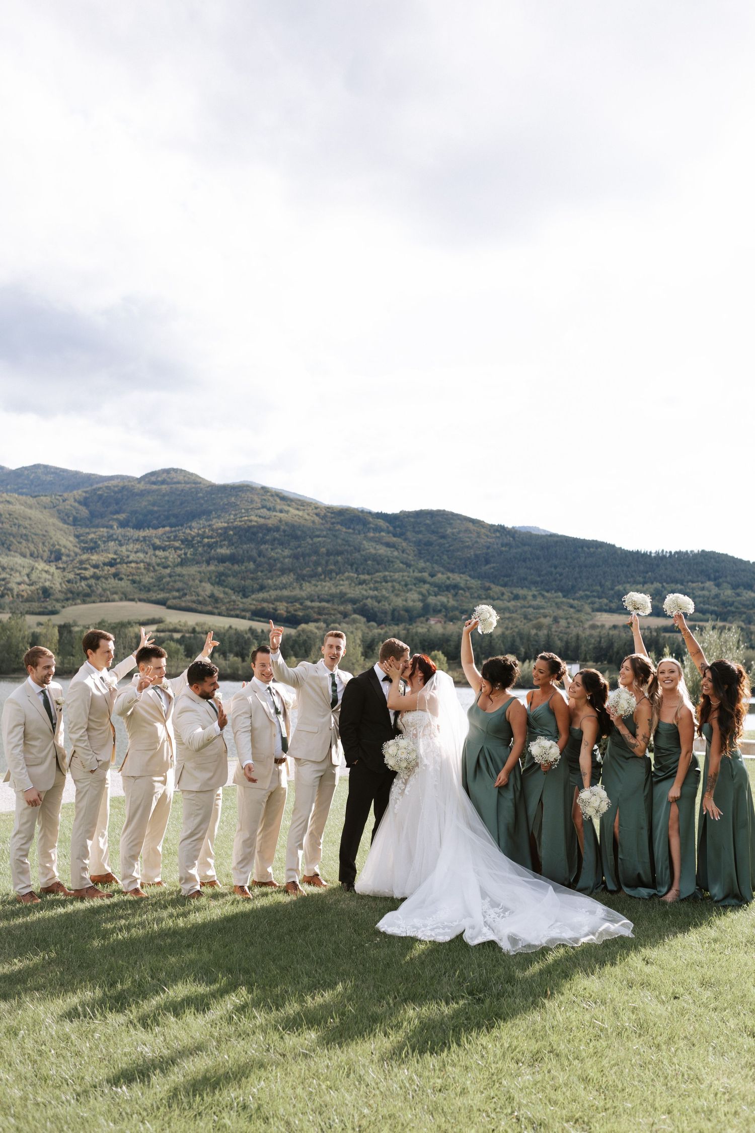 Wedding party in sage and beige attire poses against mountain landscape.